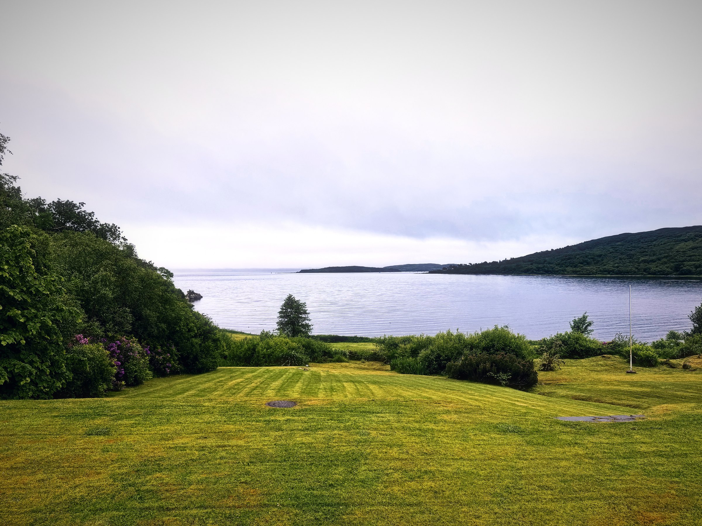 A striped green lawn rolling down to a pale silver bay and low hills.