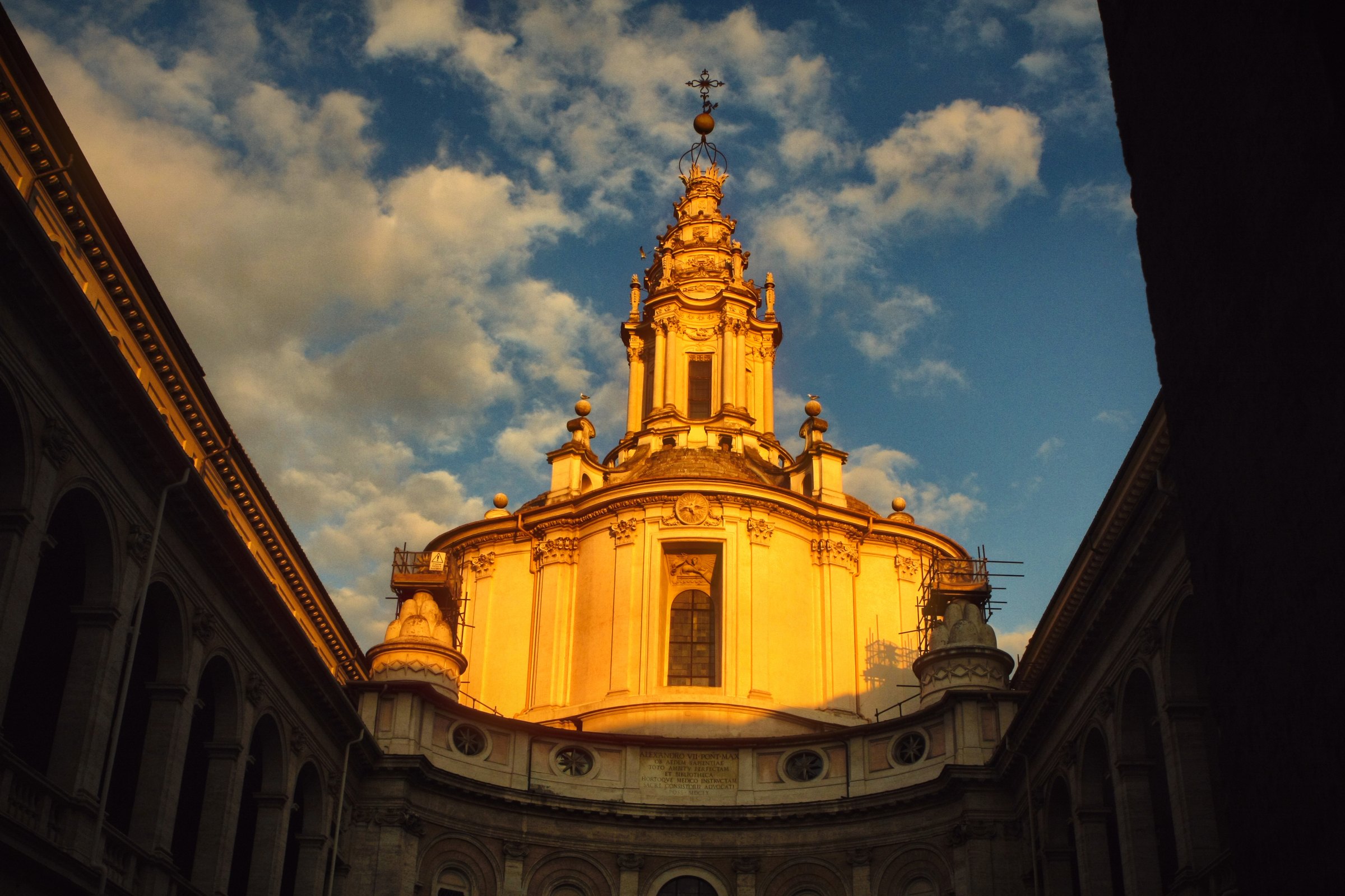 The baroque lantern of Sant'Ivo alla Sapienza glowing gold between two dark walls.
