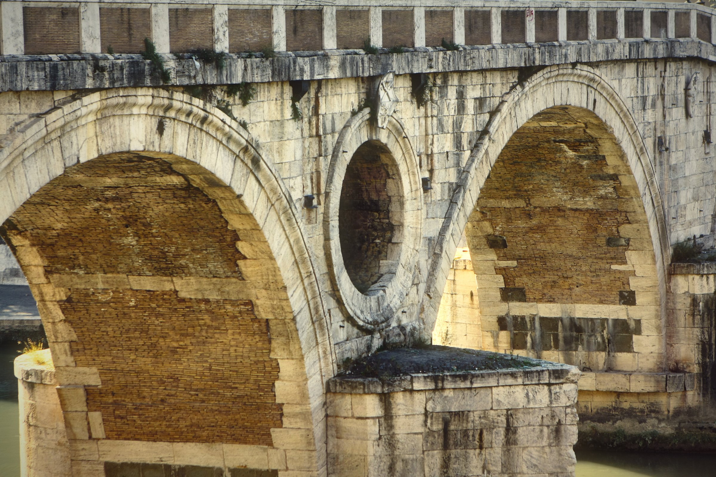 Close view of a stone bridge arch and its round opening over the river.