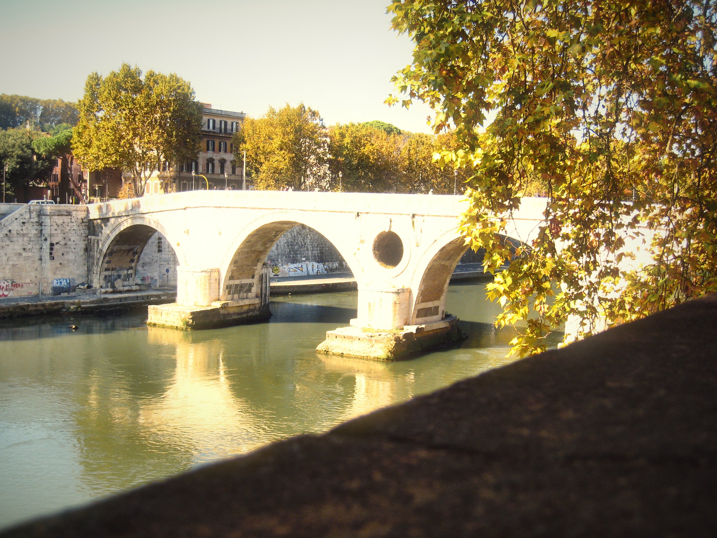 A white stone bridge over the Tiber framed by leaves.