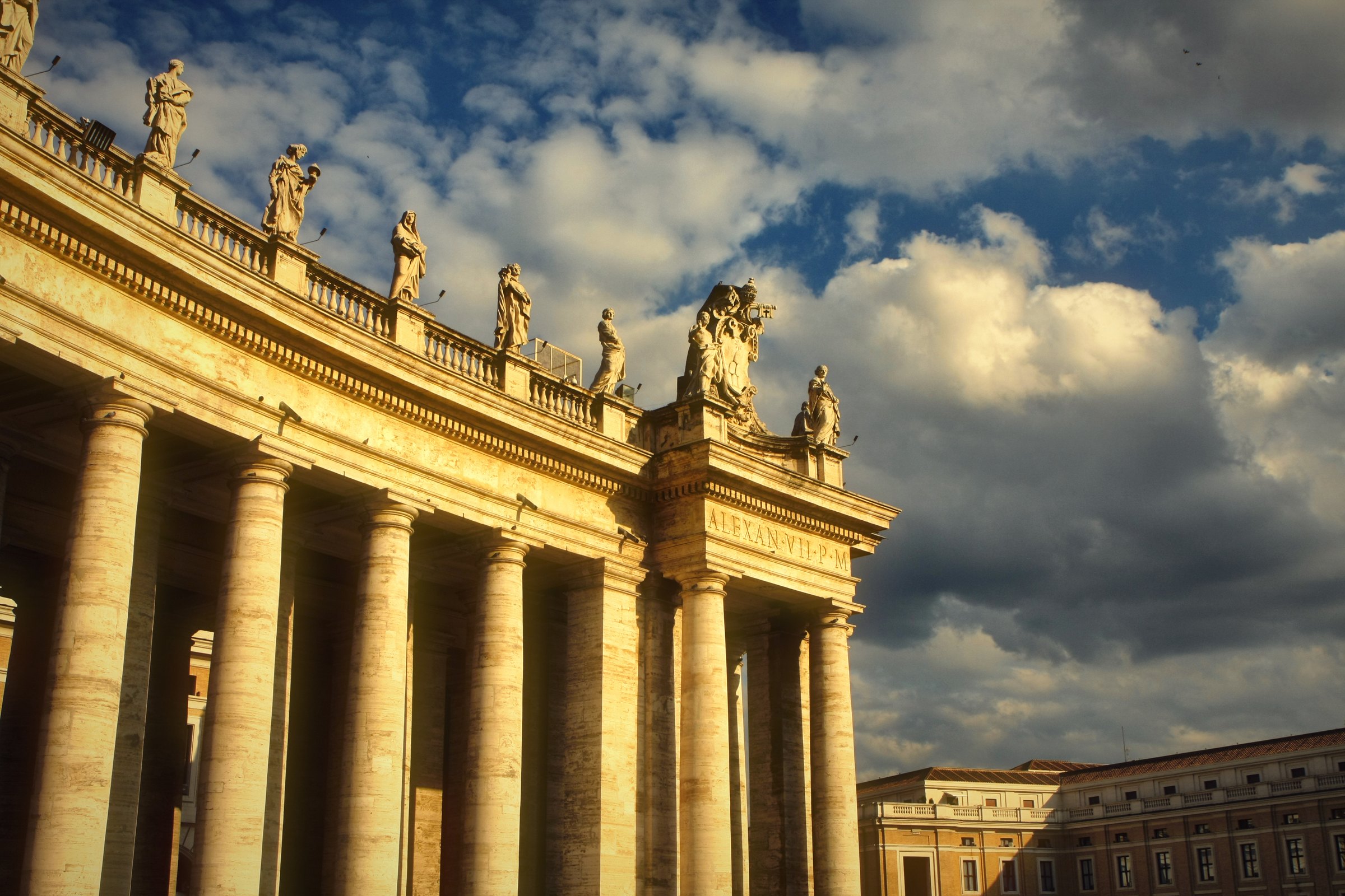 The columns and statues of St Peter's colonnade under dramatic clouds.