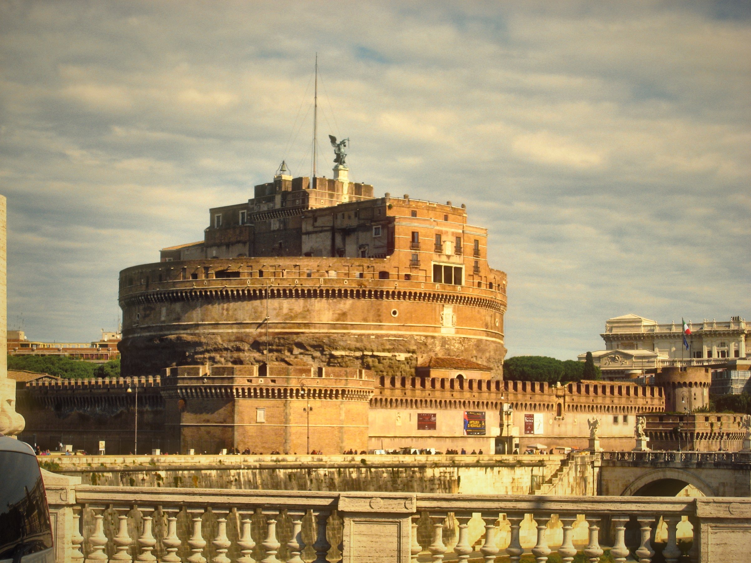 Castel Sant'Angelo under a hazy warm sky above the riverside wall.