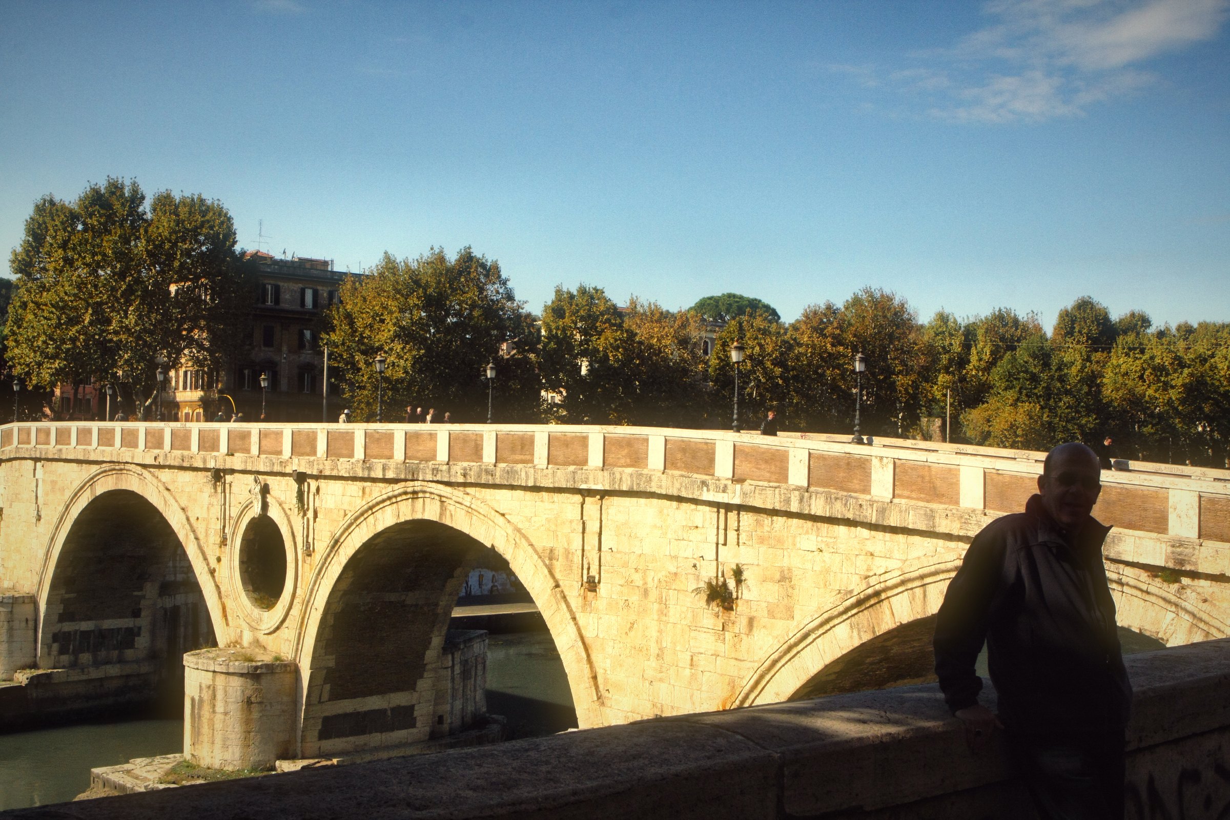 A row of stone bridge arches over the Tiber with trees behind.