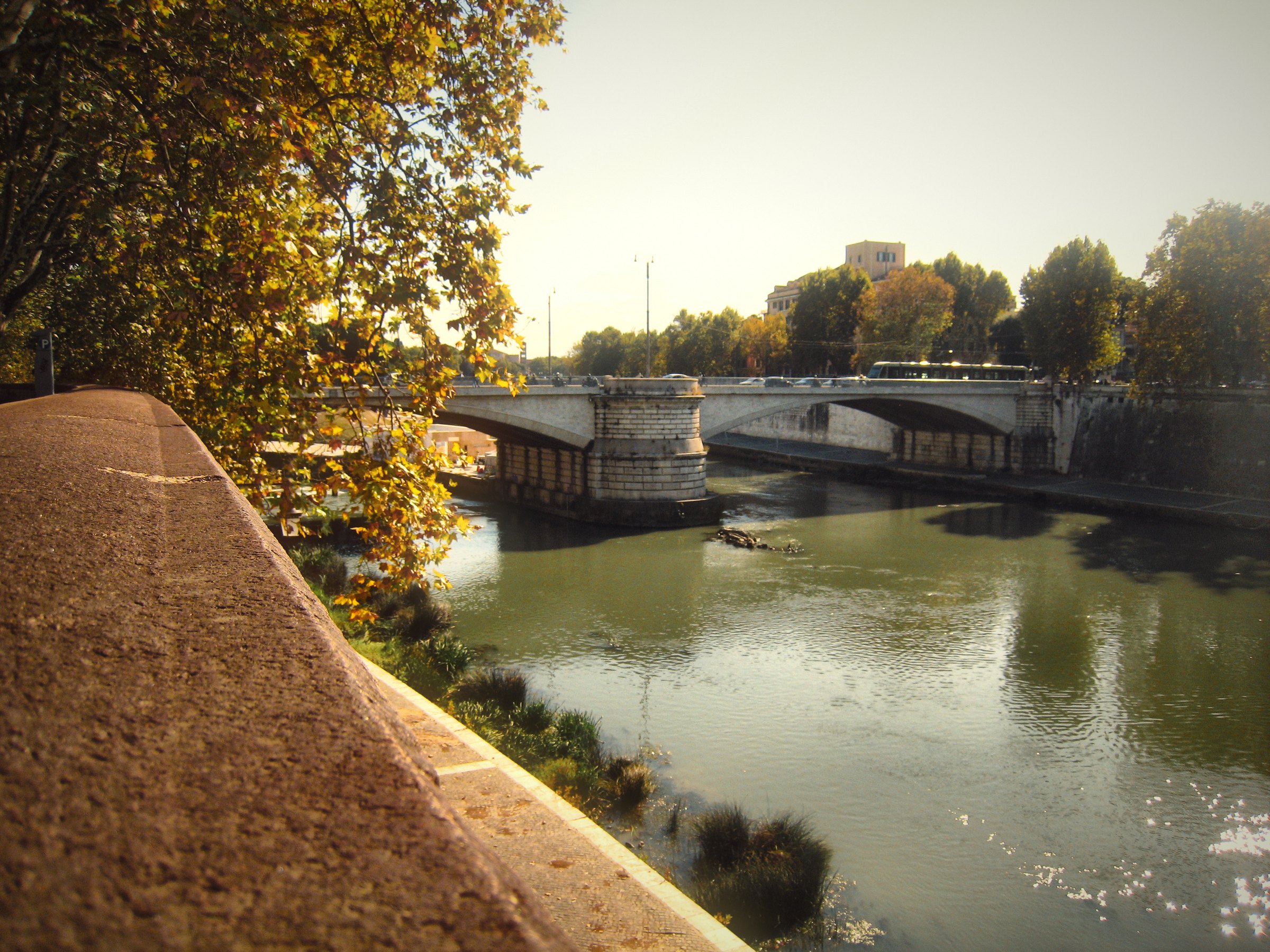 A sloping stone river wall leading to a bridge over the Tiber.
