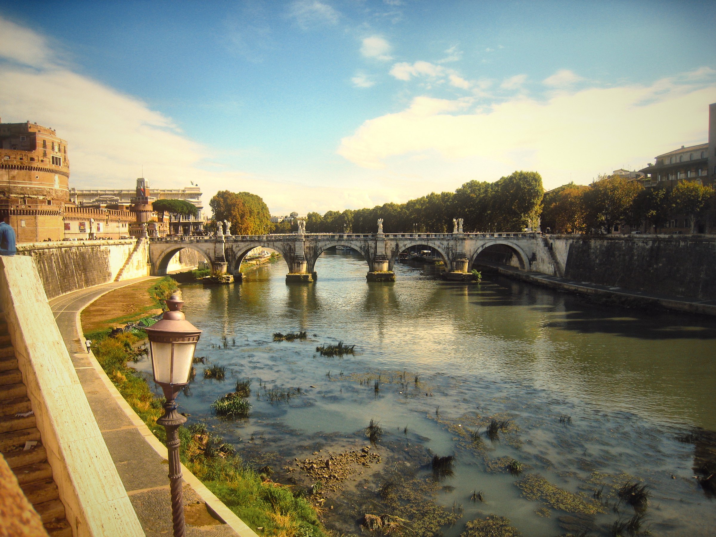 The Tiber running low between stone walls toward distant bridges.