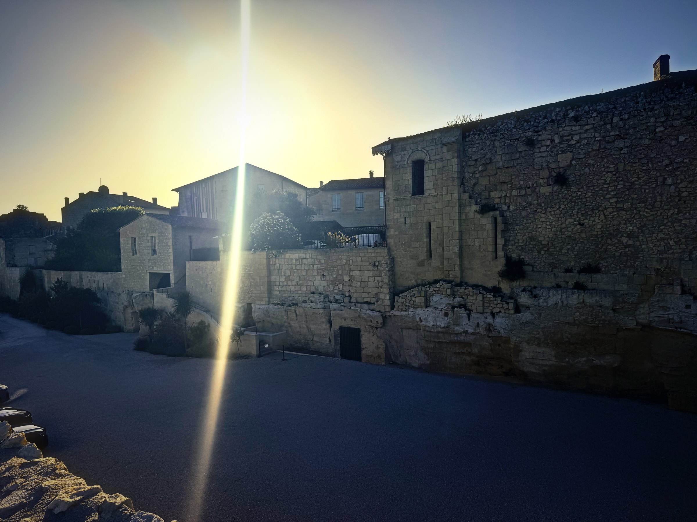 Low morning sun bursting over old stone buildings and a quiet village street.