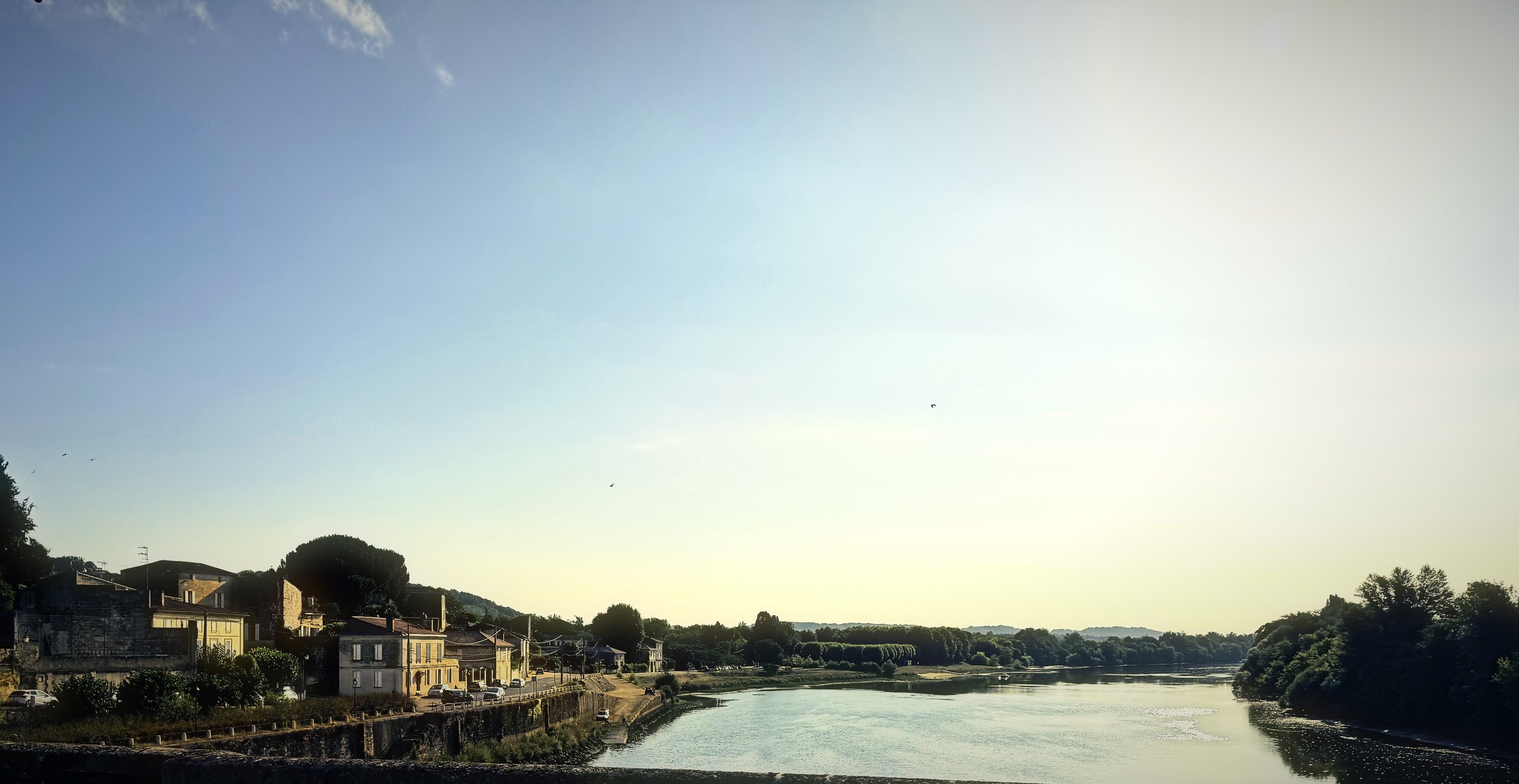 The Dordogne at Castillon-la-Bataille in early sun, with riverside houses and trees catching the light.