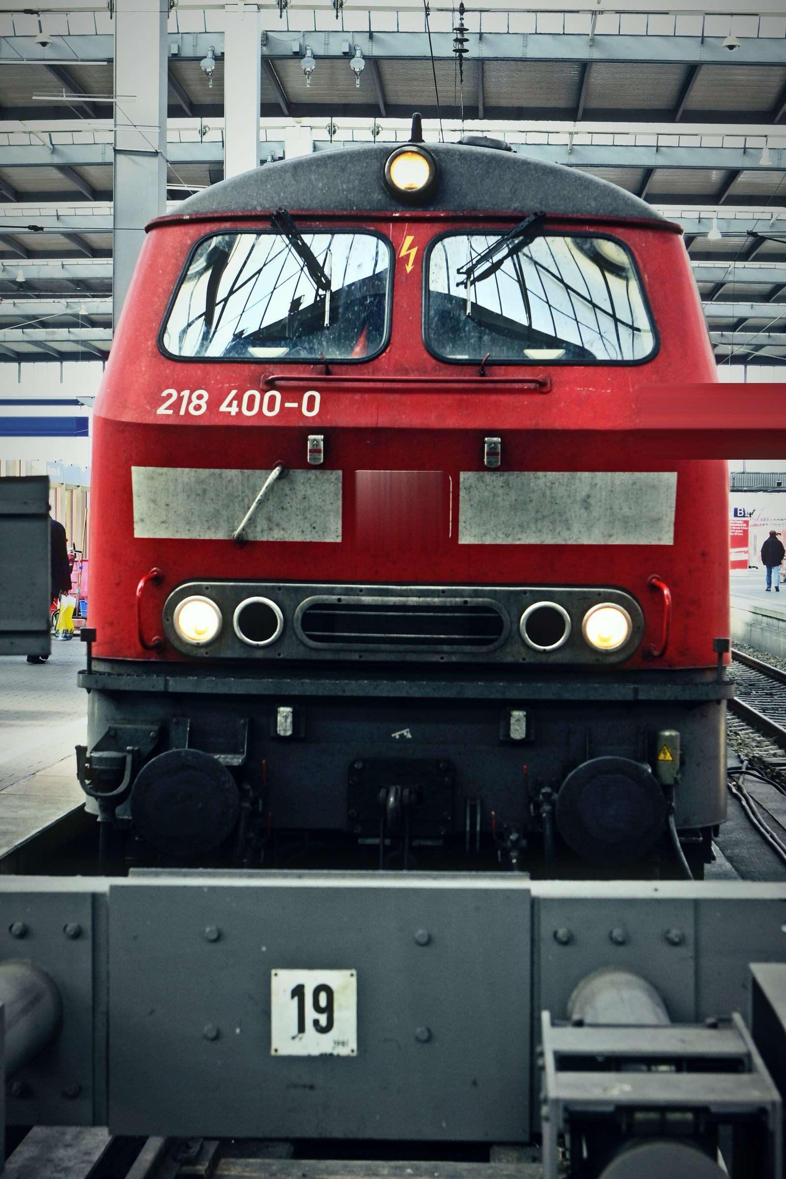 Red diesel locomotive nose-on at a platform marked 19, under a steel train-shed roof.
