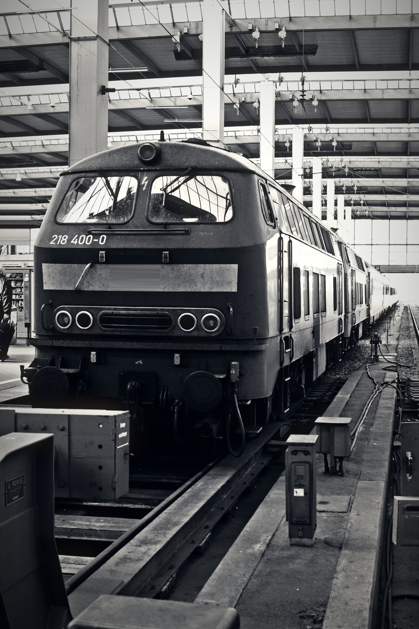 Dark diesel locomotive heading a line of coaches beneath a pale steel roof.