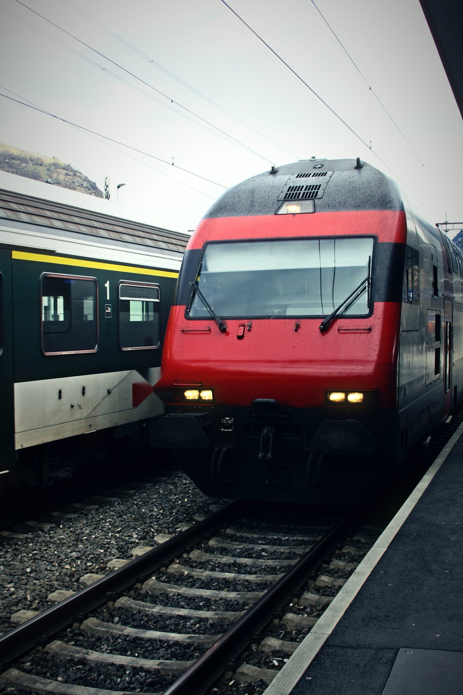 Red Swiss electric locomotive arriving at a platform beside a waiting train.