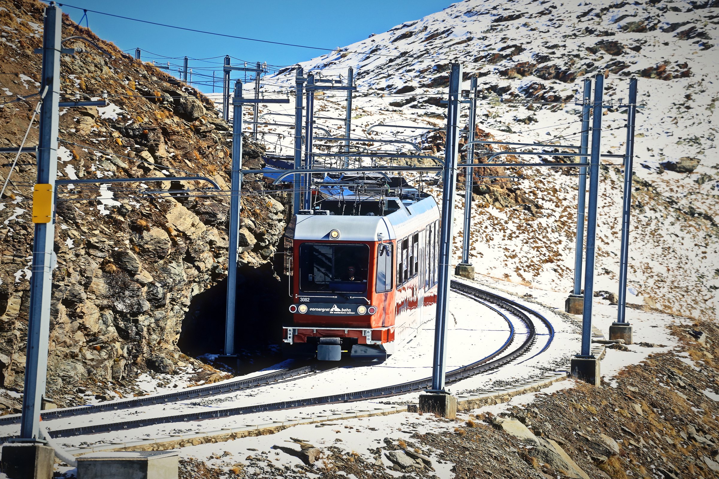Red mountain train climbing a curve through snow under overhead wires.