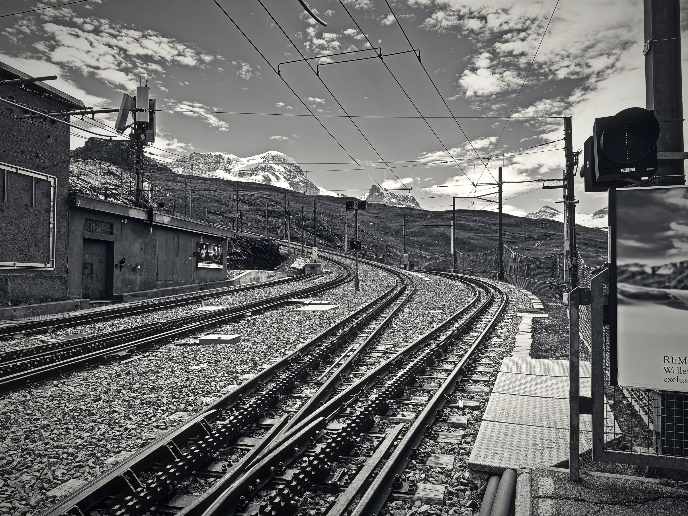 Black and white rack railway tracks curving uphill beside a small station.