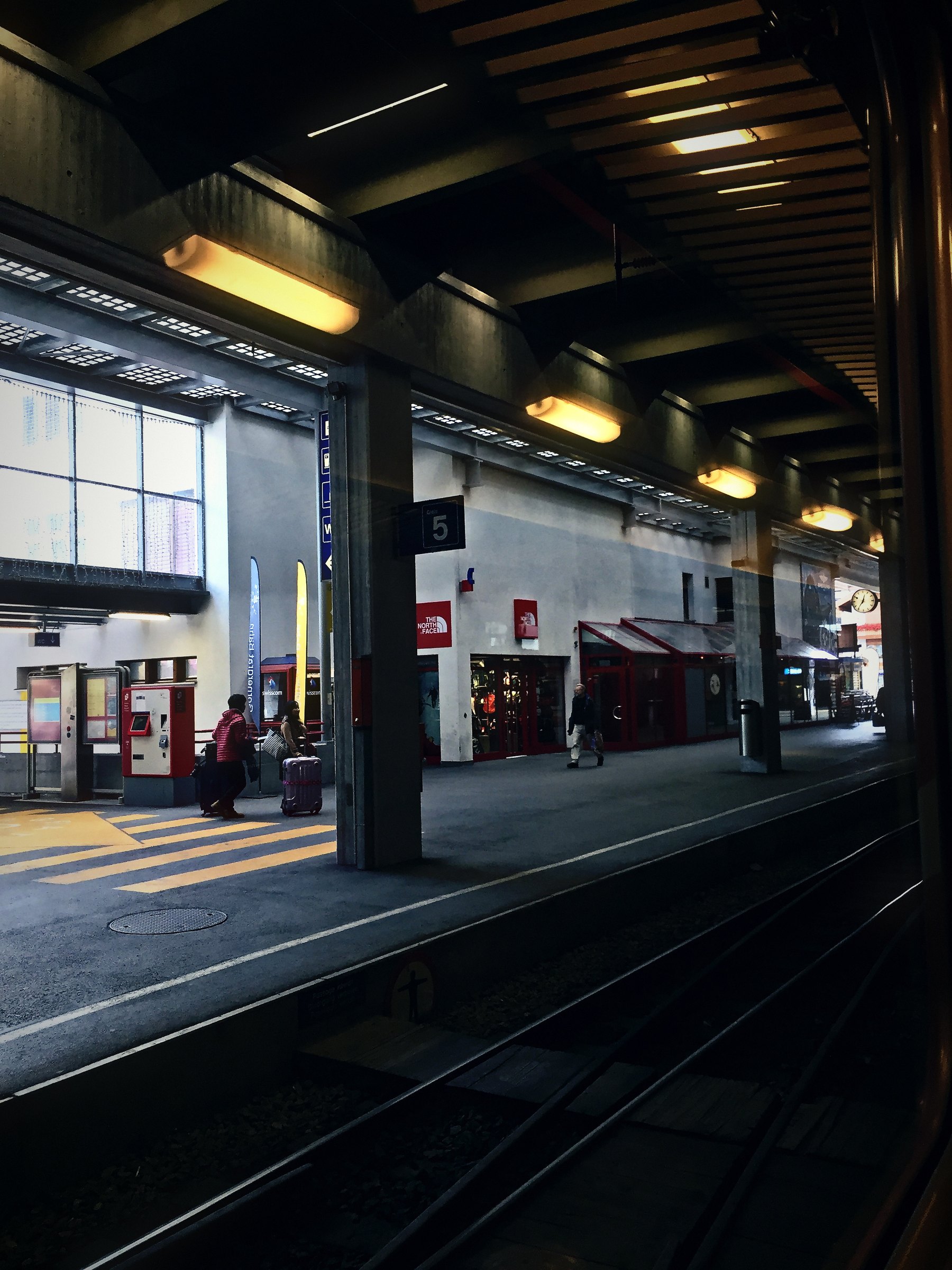 Dark station platform under a deep canopy with warm lights.