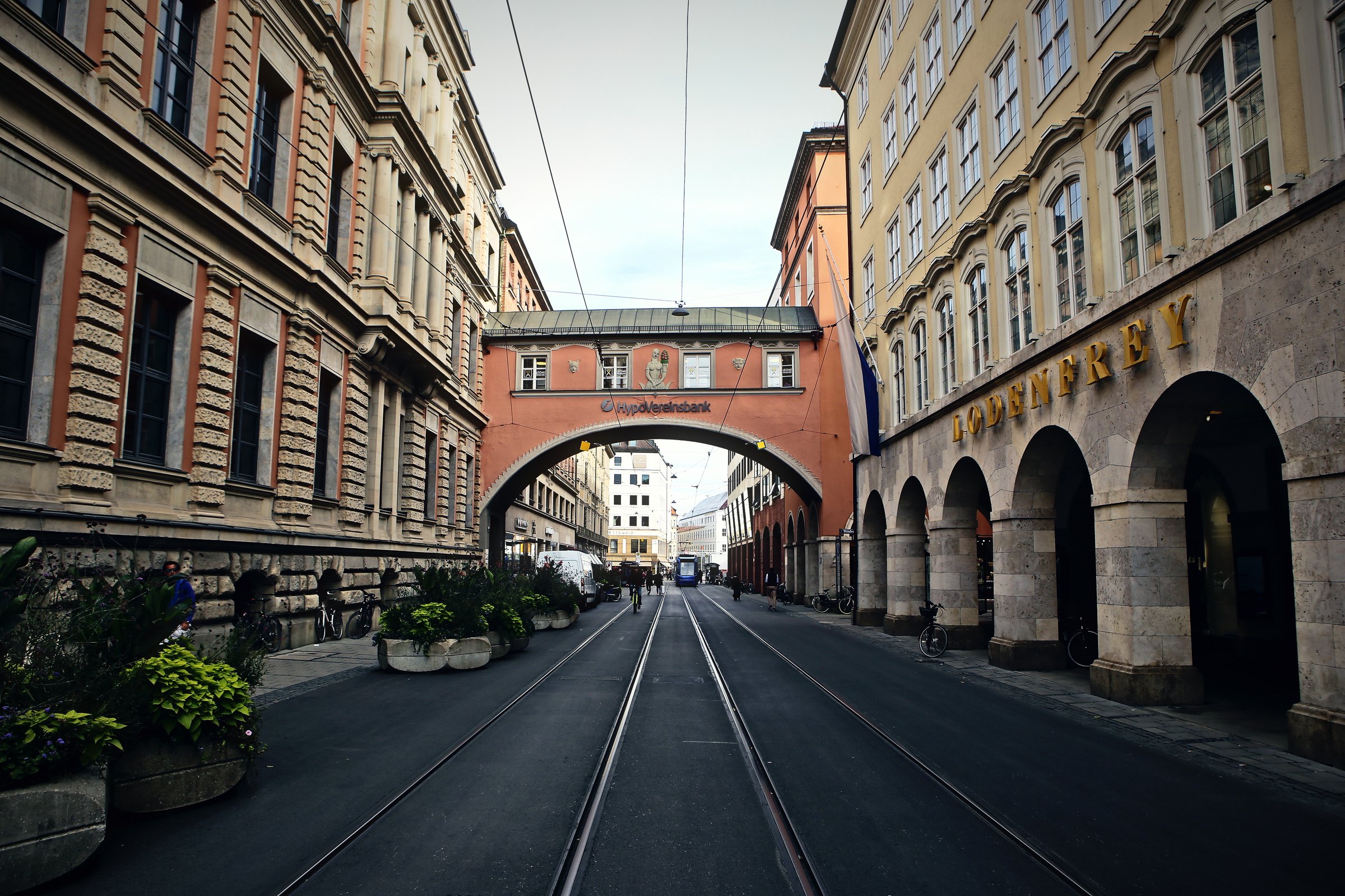 Street with tram rails running under a covered bridge between old buildings.