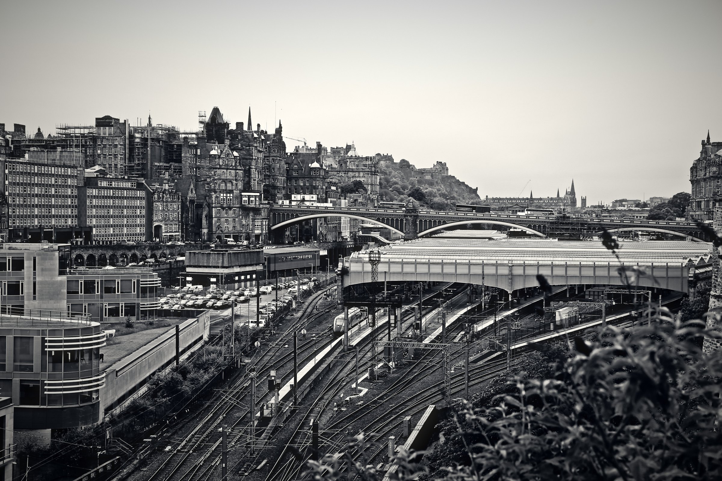 Black and white view down onto station roofs and tracks with the city skyline behind.
