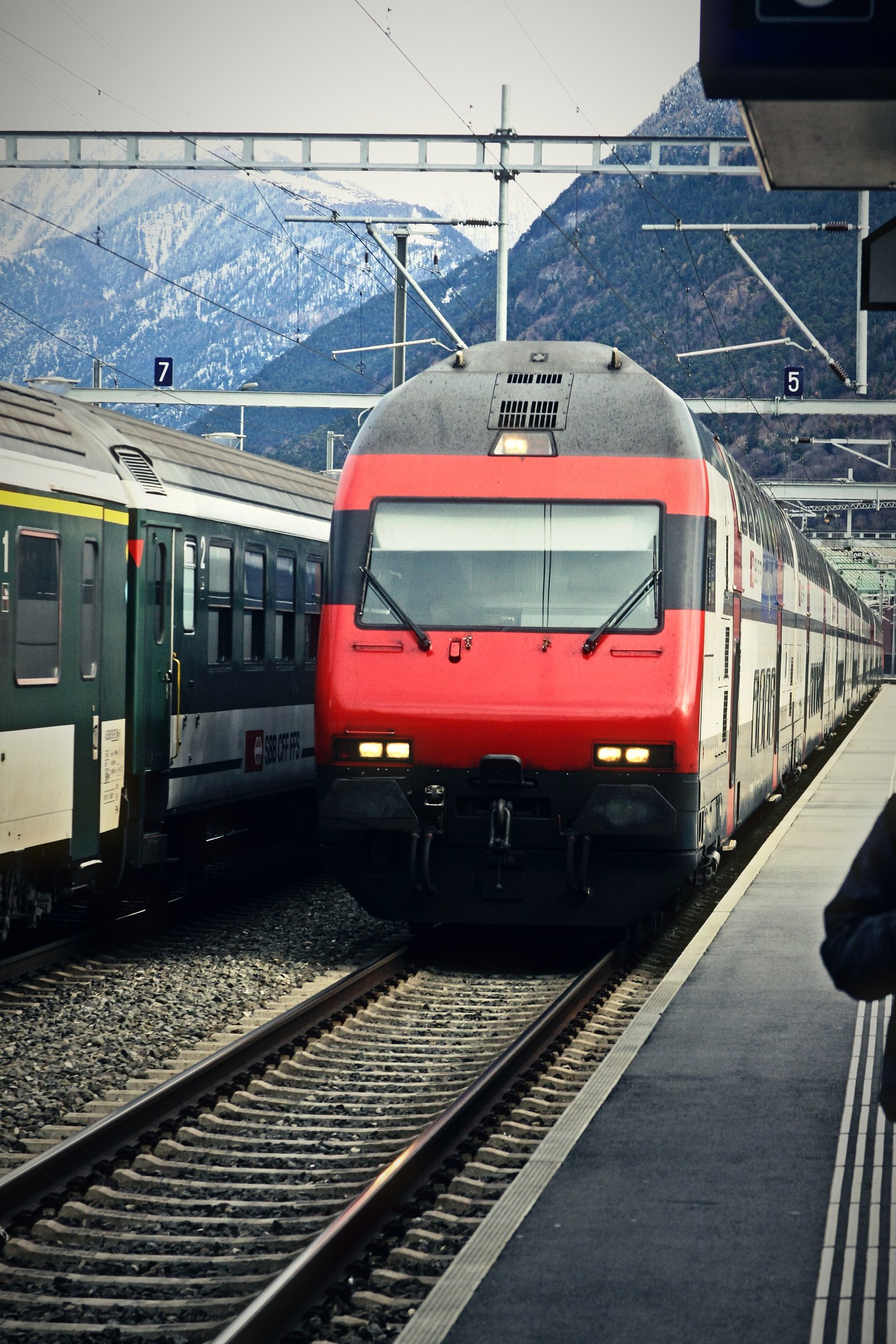 Red Swiss locomotive arriving beside another train with mountains behind.