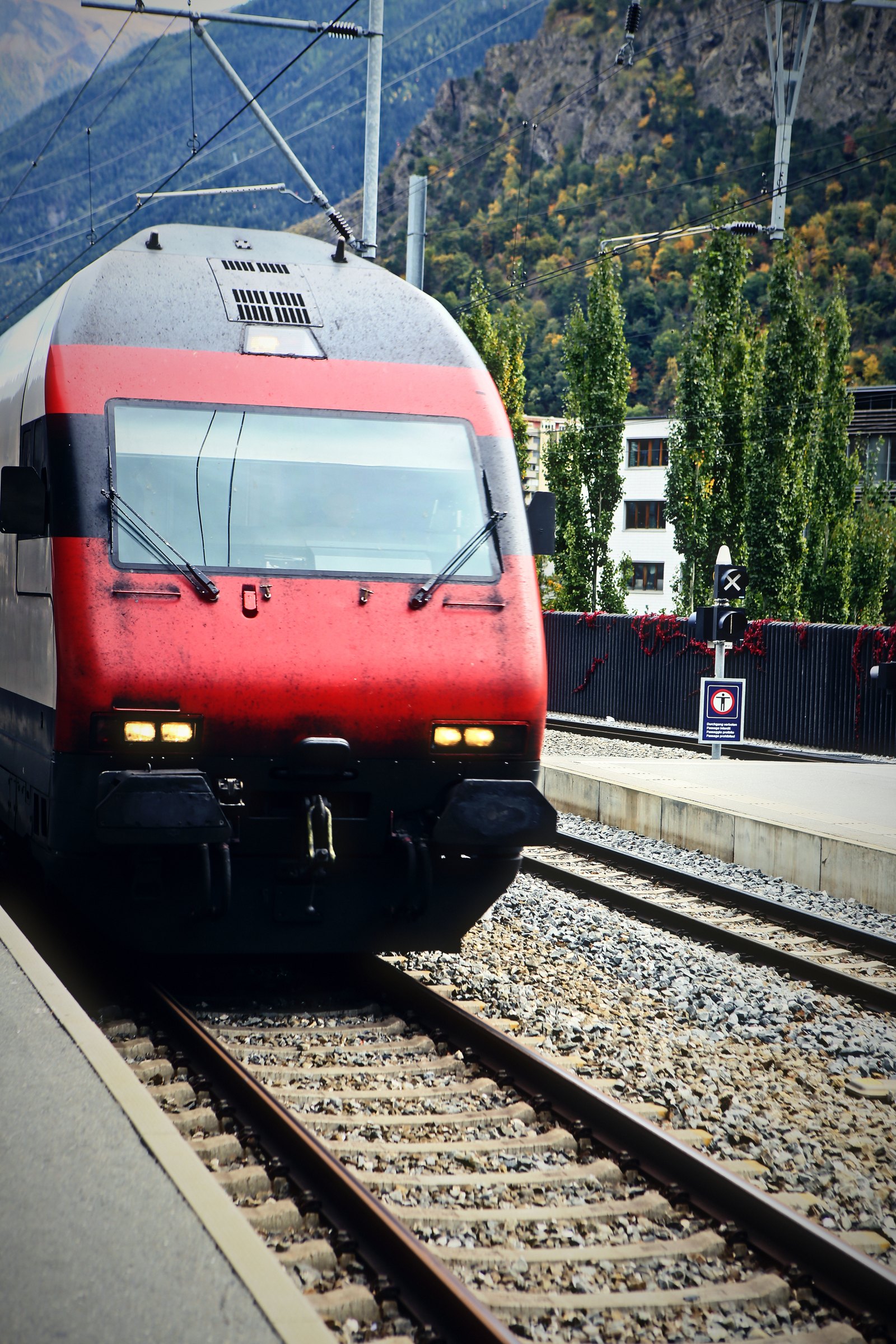 Red locomotive close up at a platform edge with steep green slopes behind.