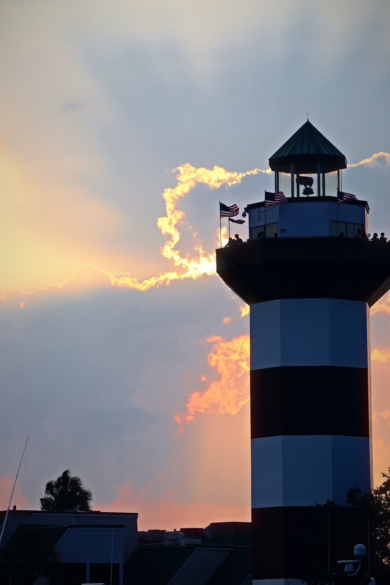 Red and white striped lighthouse against a storm cloud lit gold at the edge by evening sun.