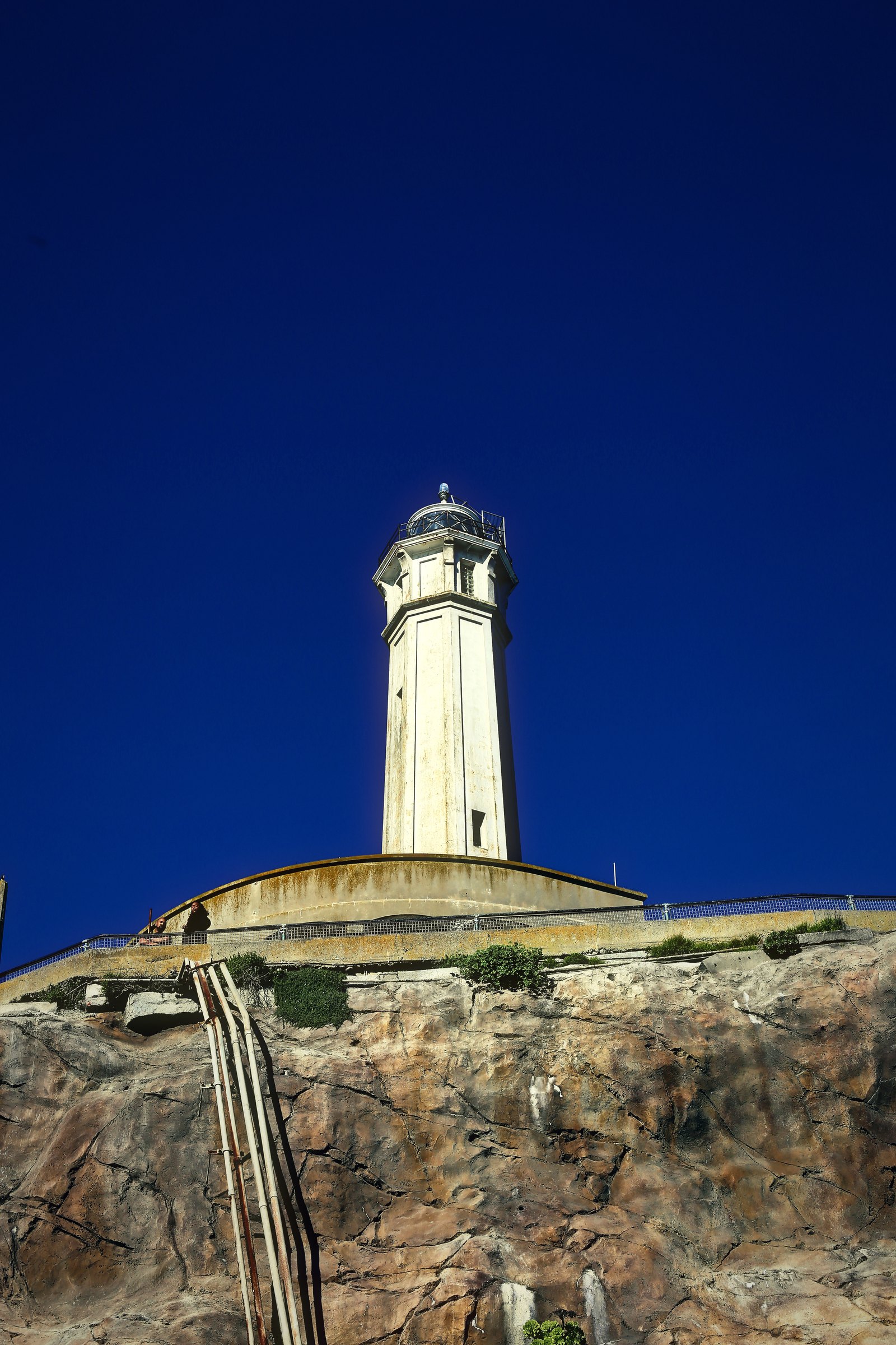 Lighthouse over old concrete walls and rock under a deep blue winter sky.