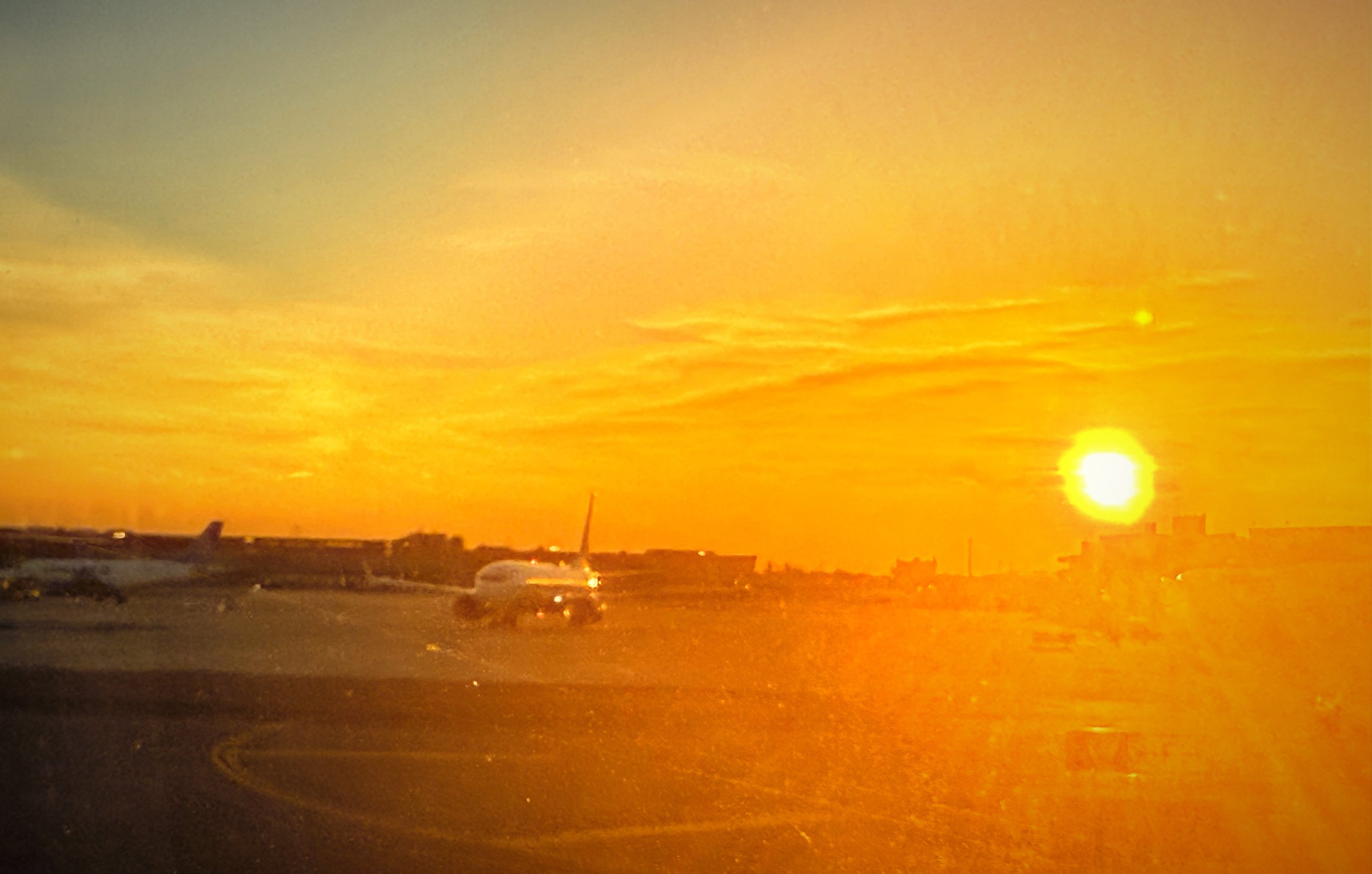 A jet on an airport taxiway under a wide orange sky with the sun hanging low.