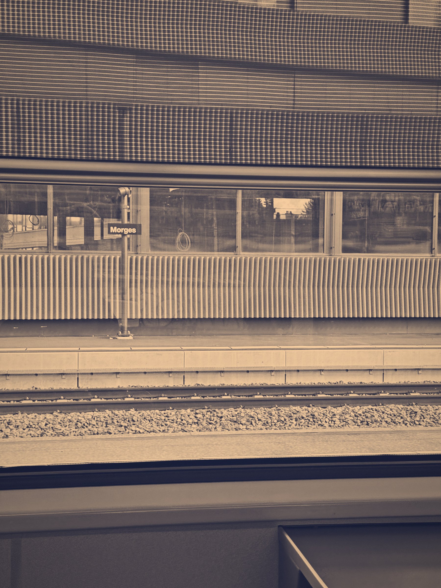 Duotone of a station building facade, fence and tracks in warm grey and amber.