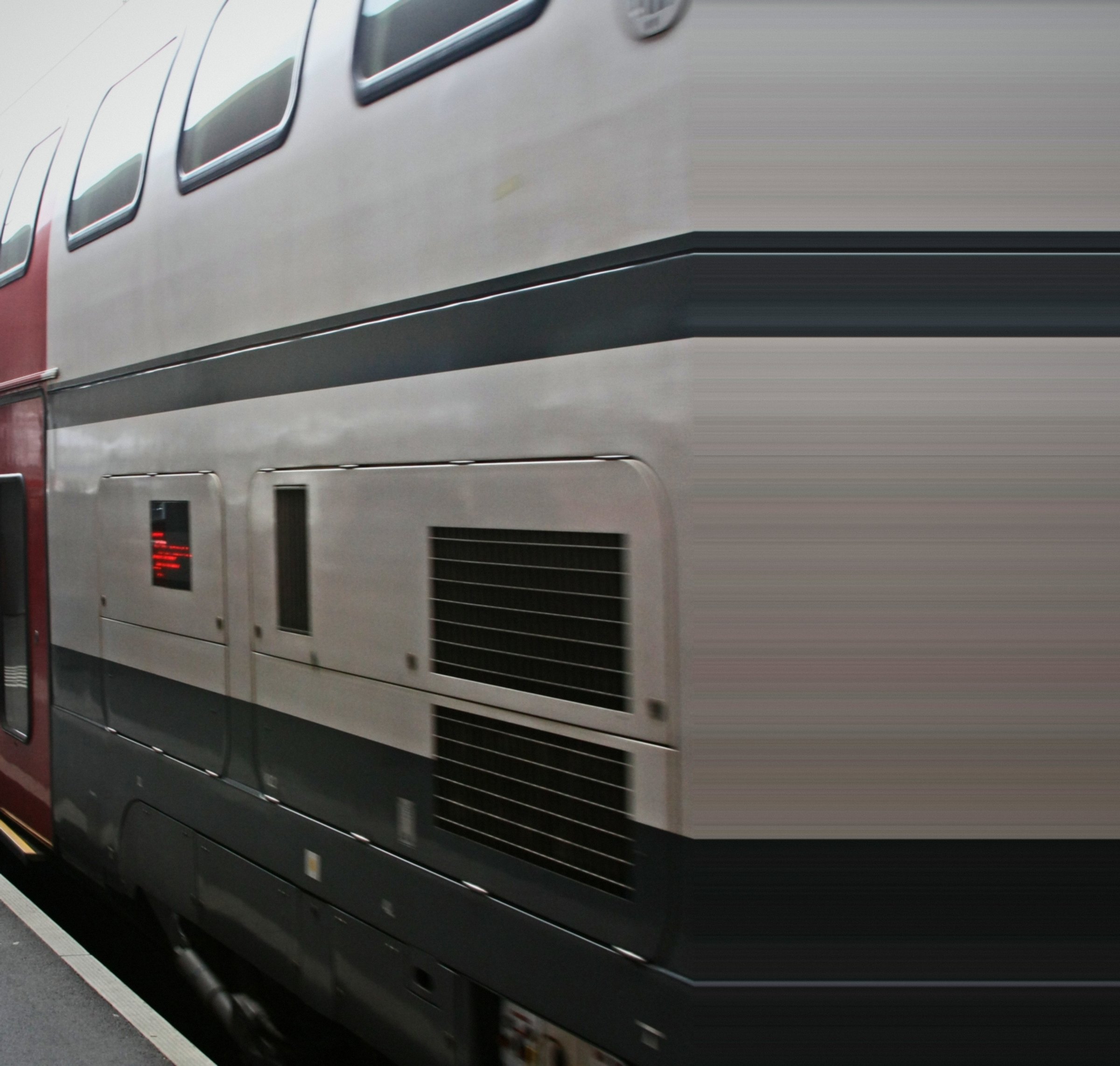 Close abstract of a silver double-deck carriage side with dark bands and vents.