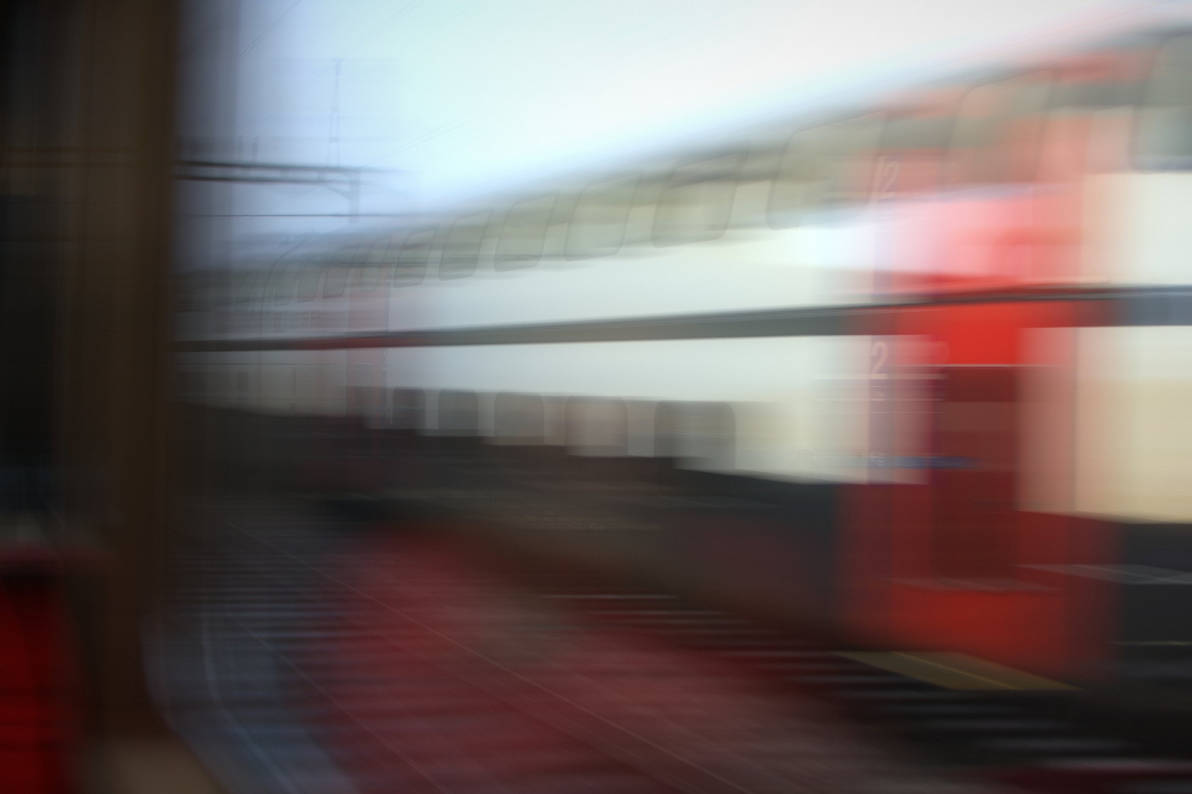 Radial blur of a red and white train leaving a platform.
