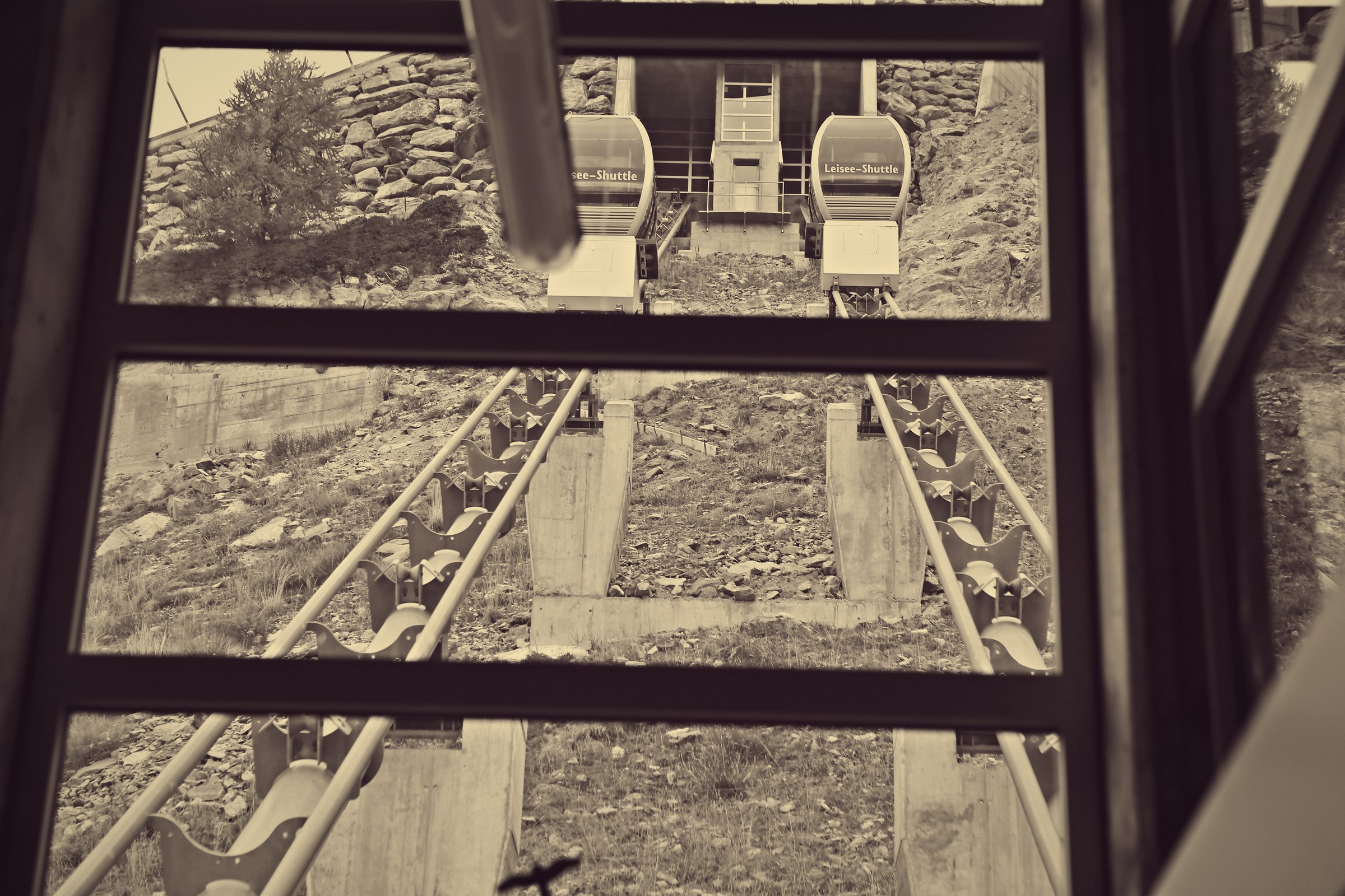 Sepia view through a funicular window down onto parallel tracks and passing cars.