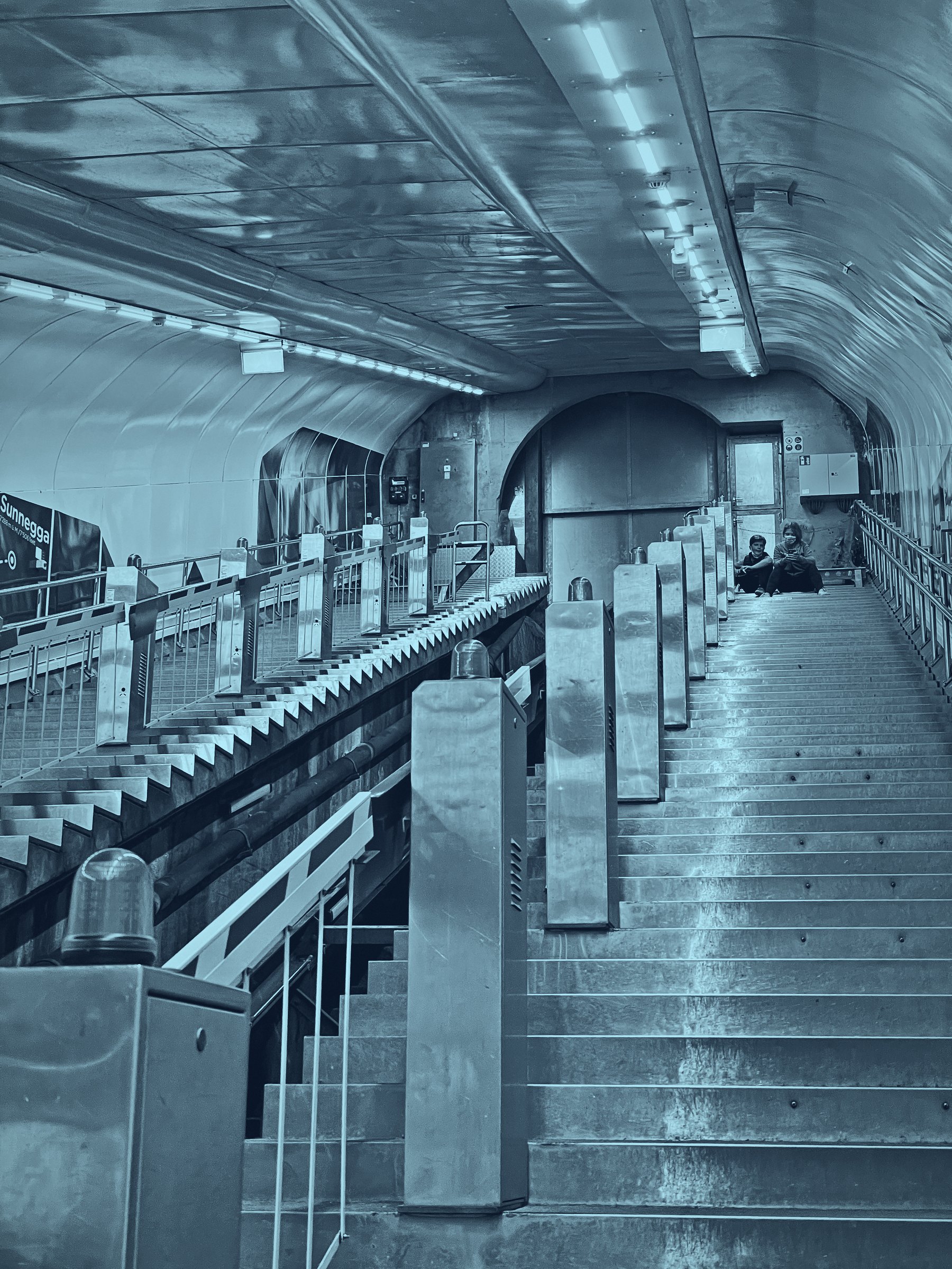 Cold blue duotone of a long staircase and tunnel in a funicular station.