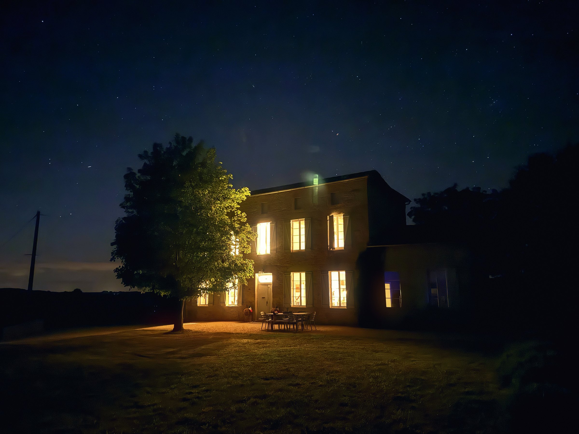 A stone country house with its windows glowing gold beneath a deep blue starry sky.