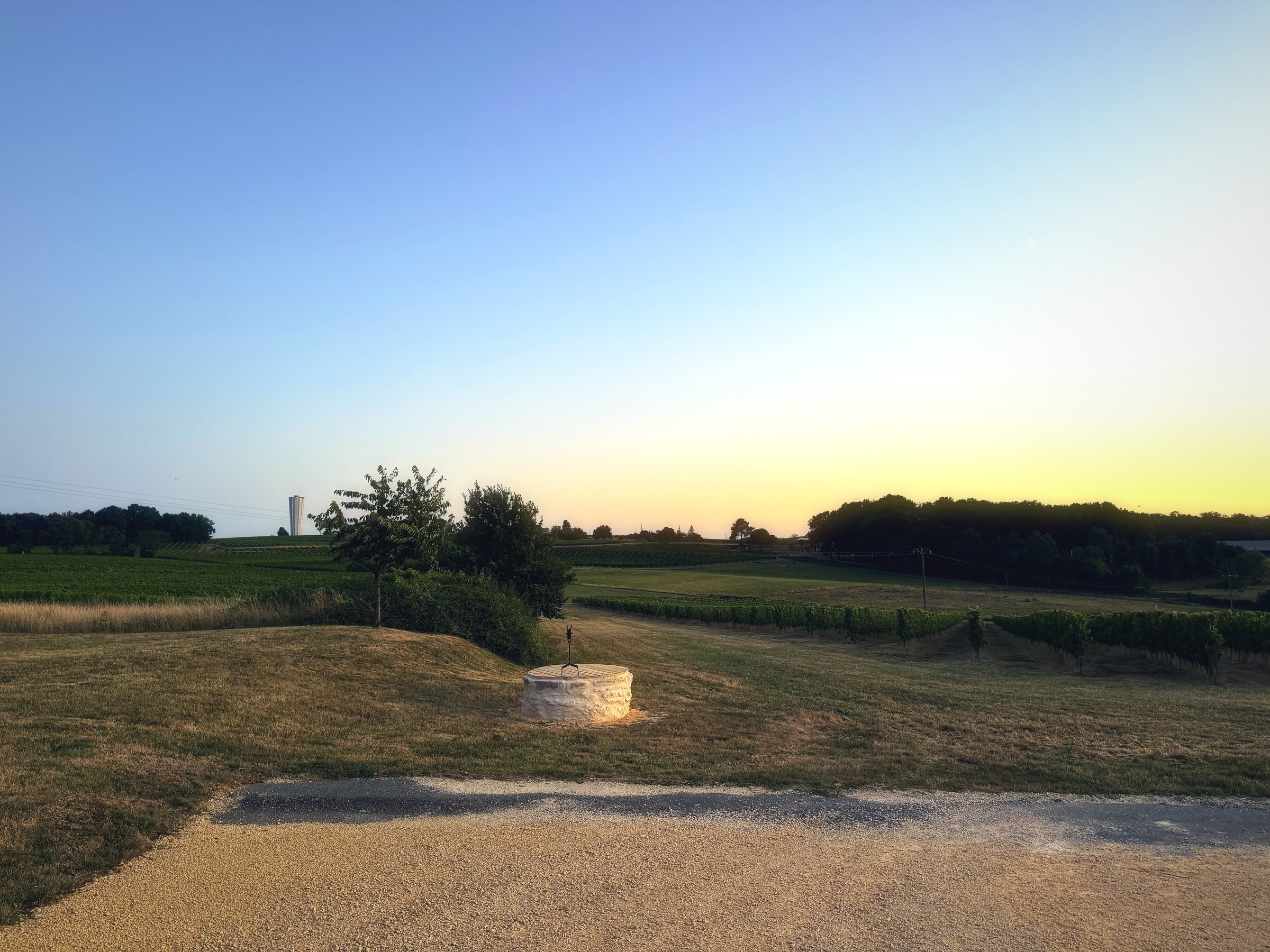 A pale band of afterglow over a dry field, a low wall and a distant tree line.