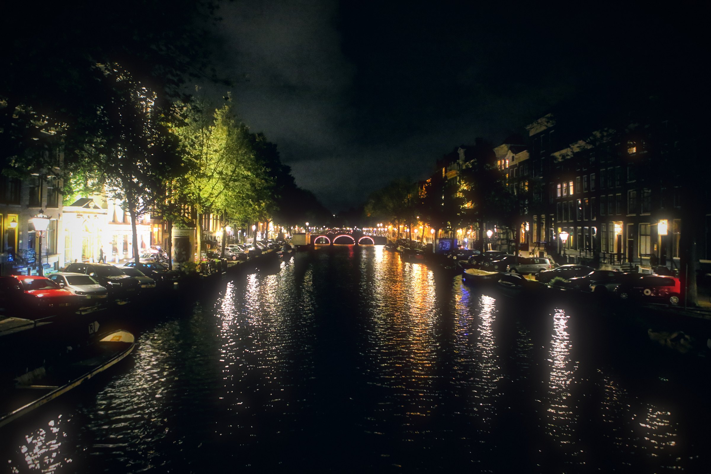 An Amsterdam canal at night with lights reflected in long streaks.