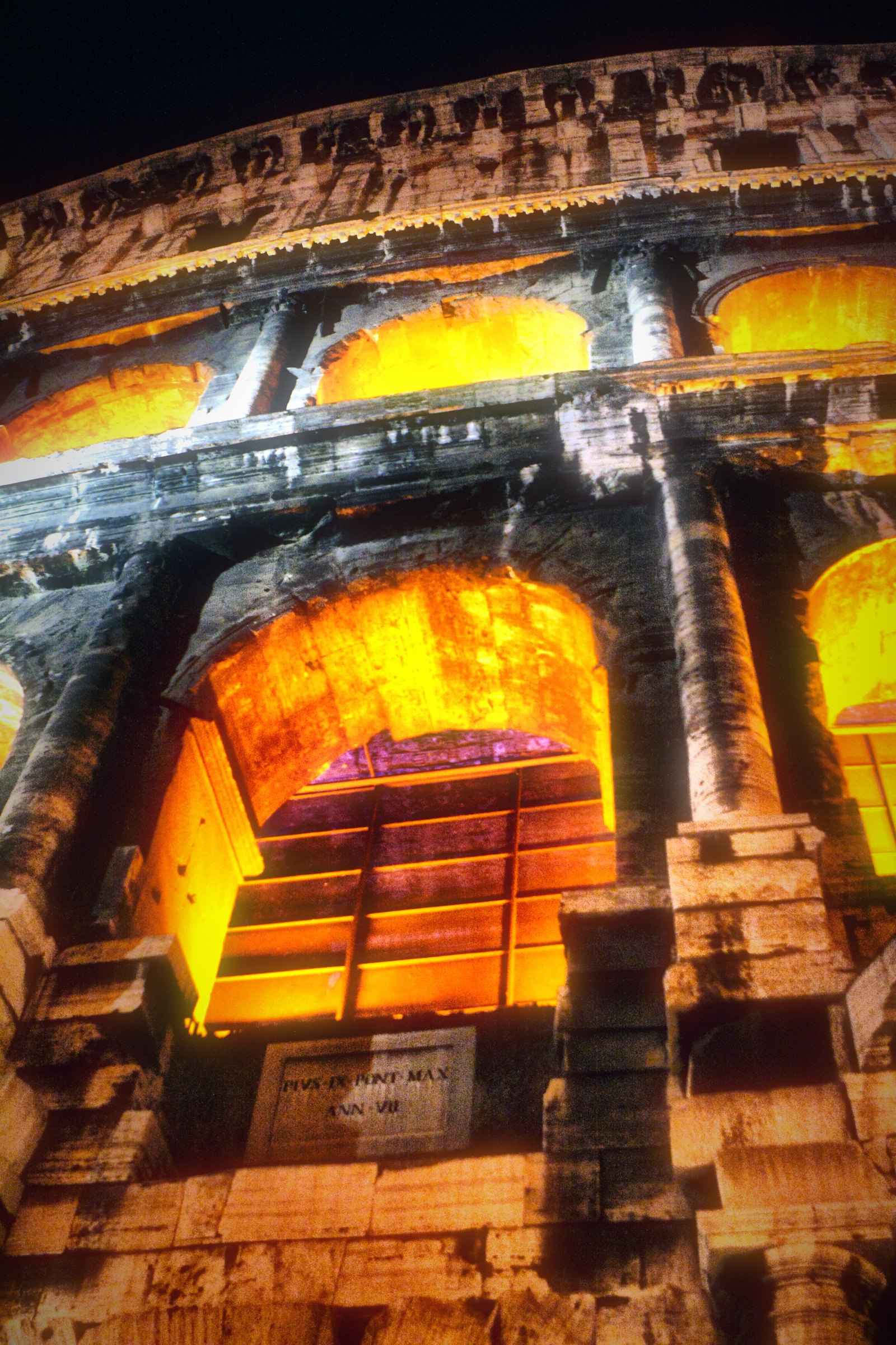 A close view of the Colosseum's arches glowing orange at night.