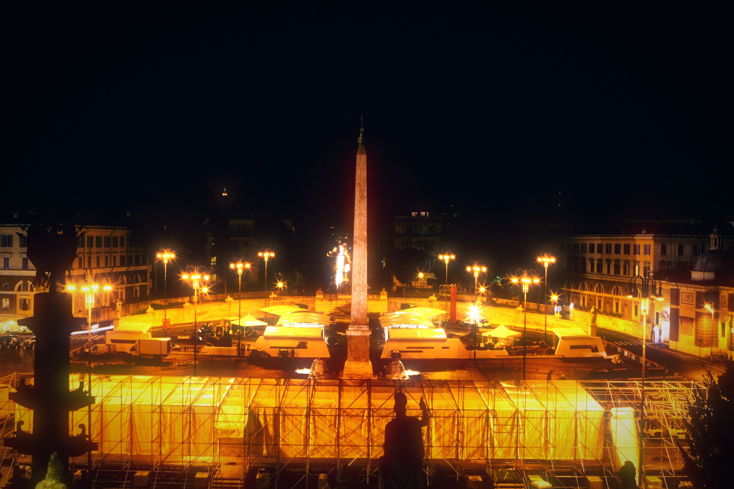 Piazza del Popolo at night with its obelisk and a sweep of lights.