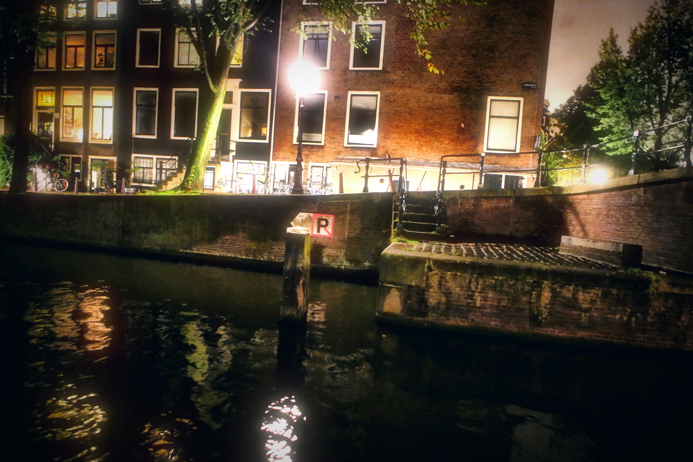 Canal houses at night with lit windows doubled in the water.