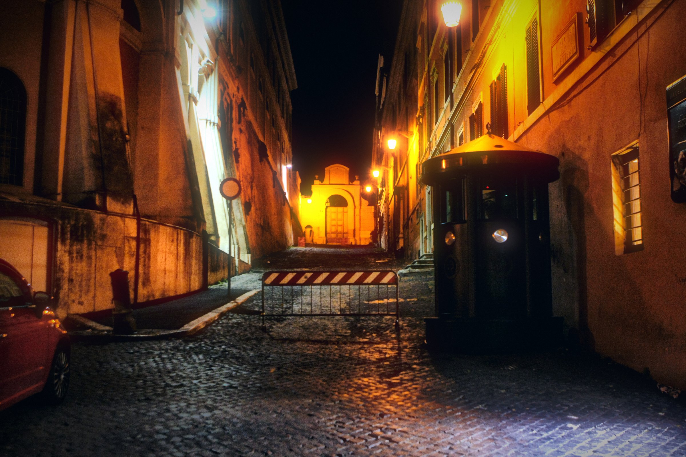 A narrow Roman lane at night with warm walls and a lit doorway.
