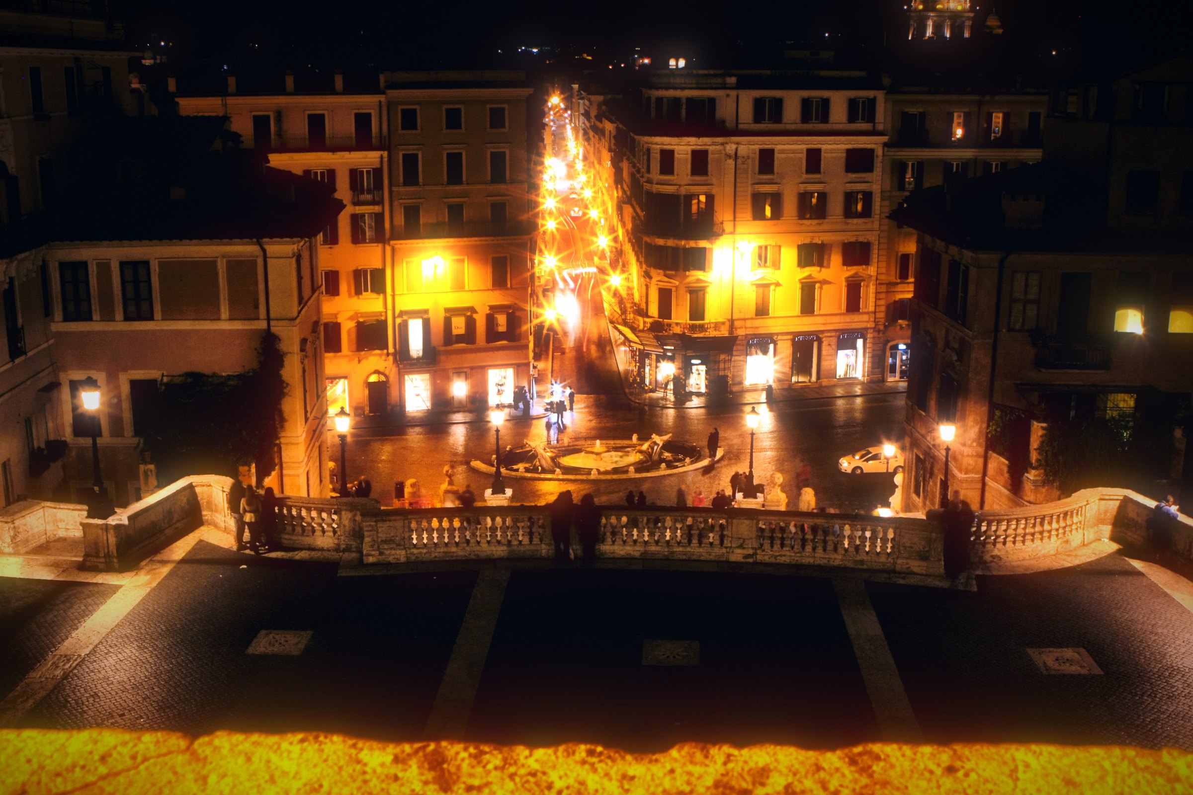 Looking down from a terrace onto a lit street at night.