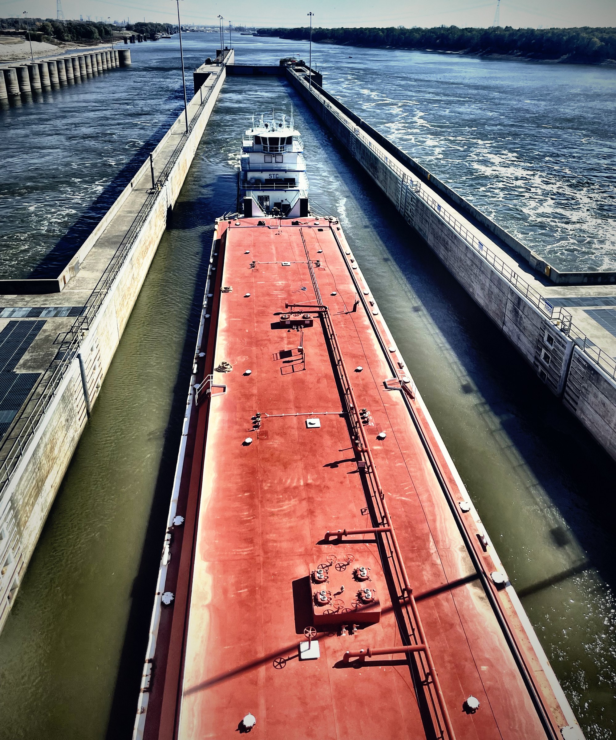 A long red barge squeezed between the concrete walls of a river lock.