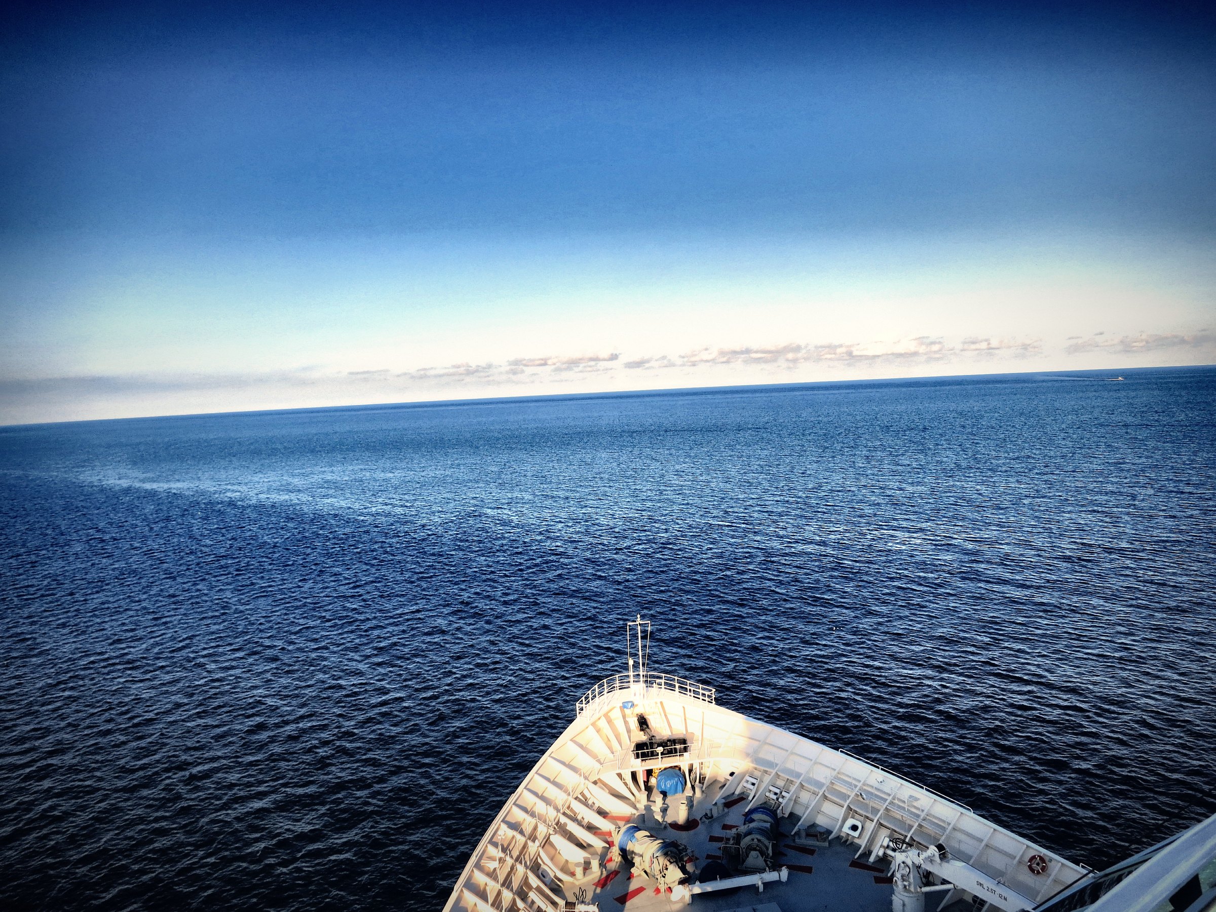 A white ship's bow pointed at a deep blue sea and a hazy horizon.