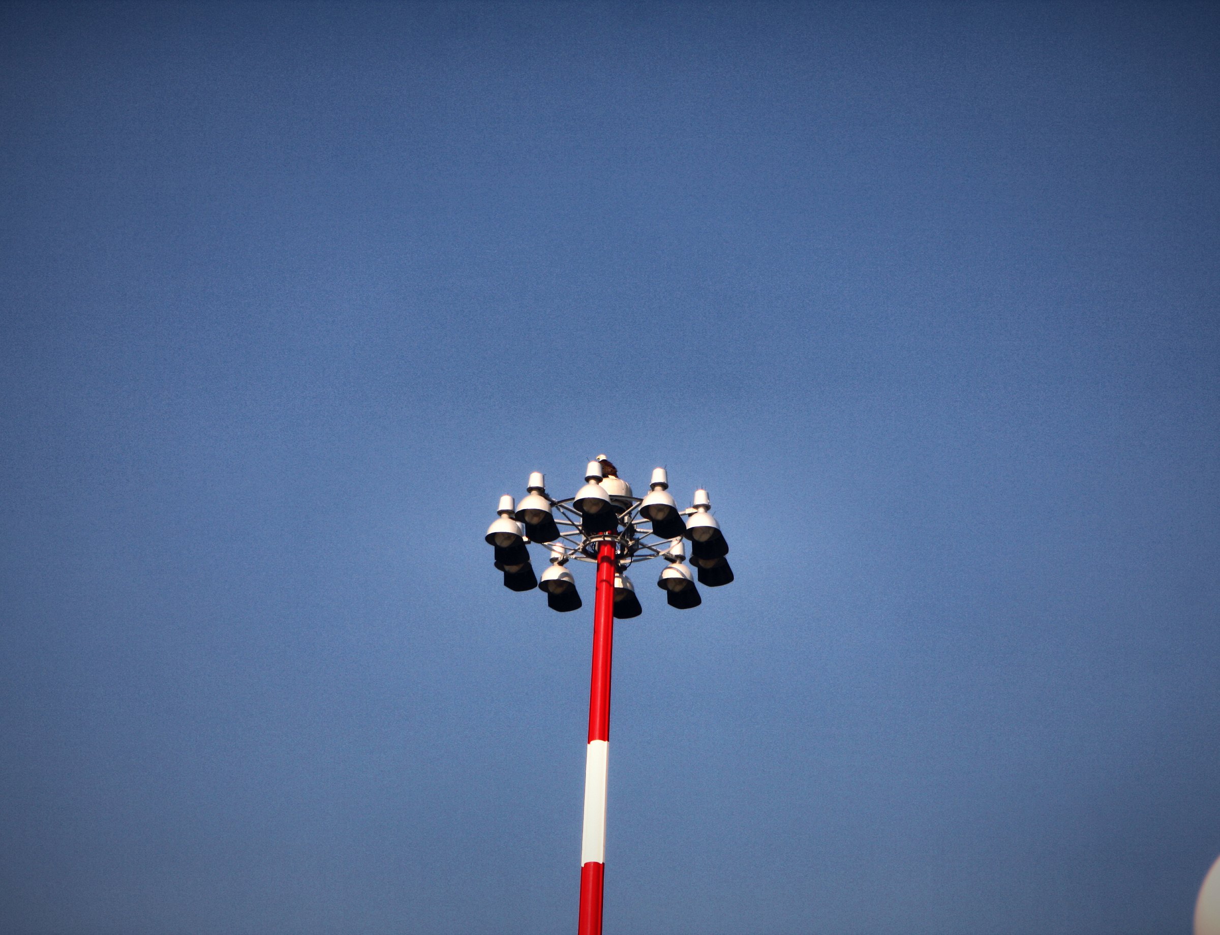 A red-and-white striped floodlight mast against a flat blue sky.