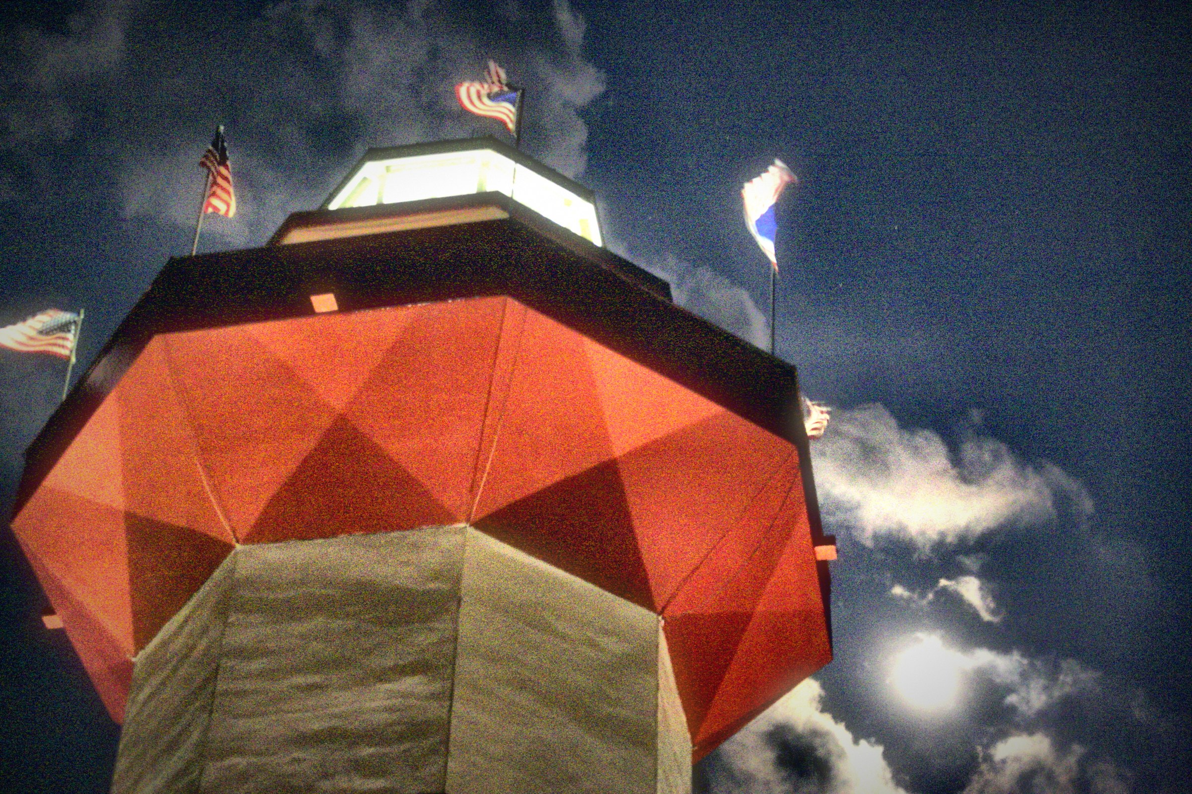 A faceted red-paneled tower crowned with flags under a dark, stormy sky.