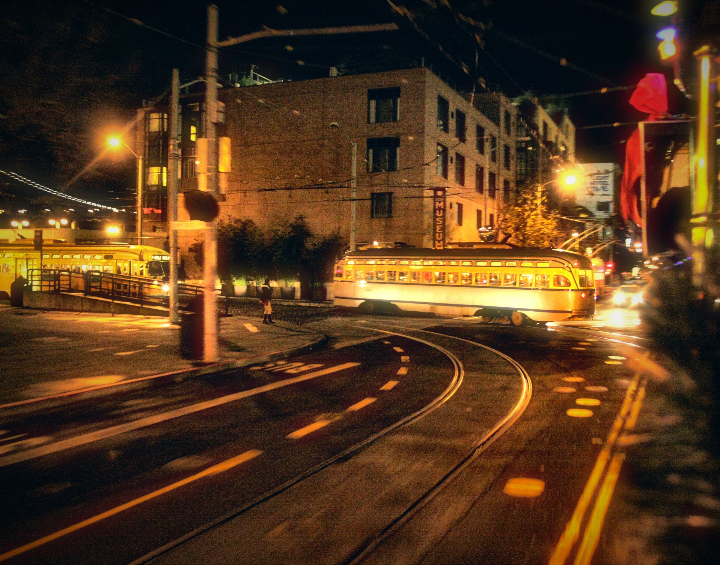 A vintage streetcar glowing gold as it curves across tracks on a city street at night.