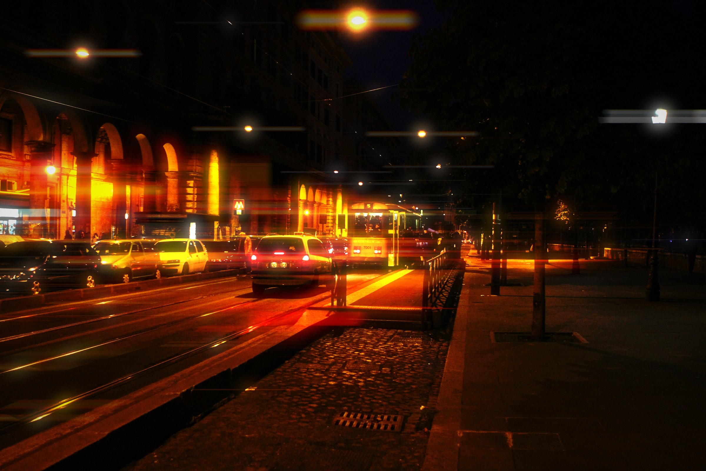 Night avenue streaked in orange and red light with arched buildings behind.
