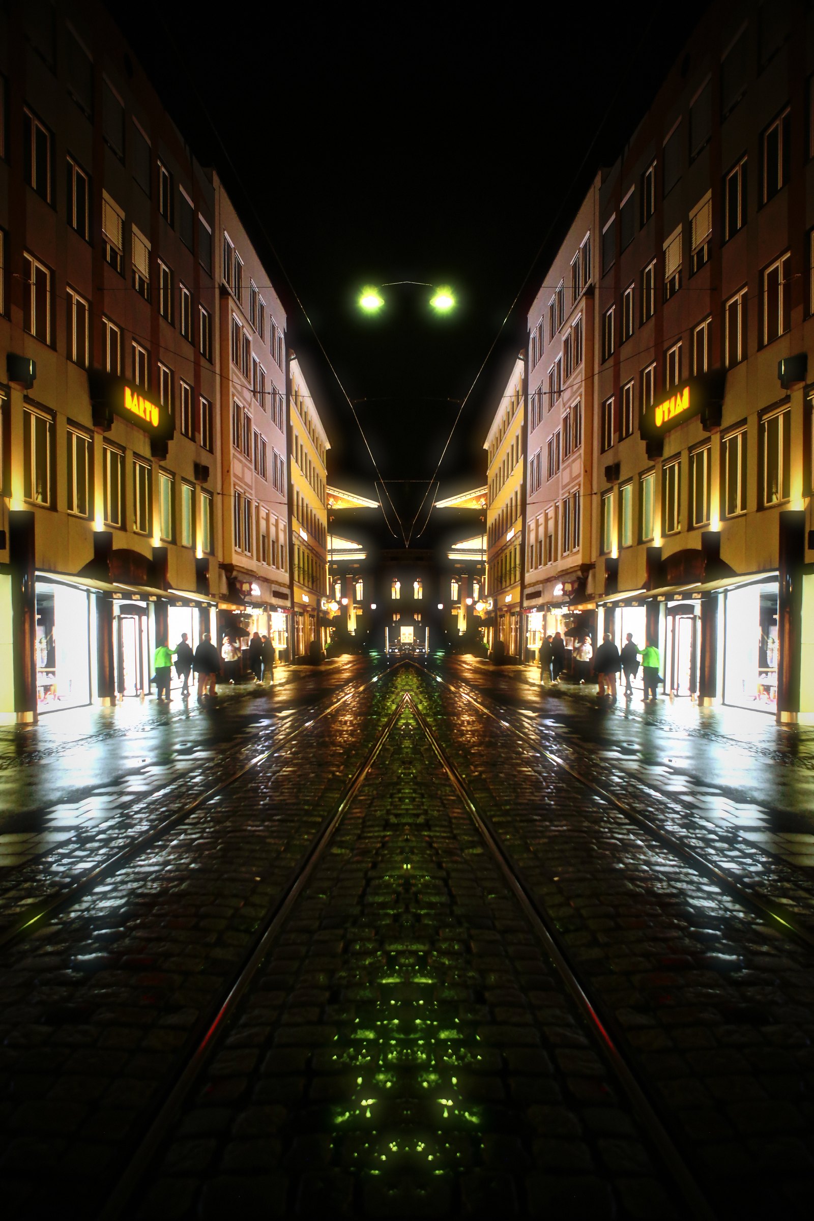 Symmetrical mirrored night street with tram rails meeting in the middle.