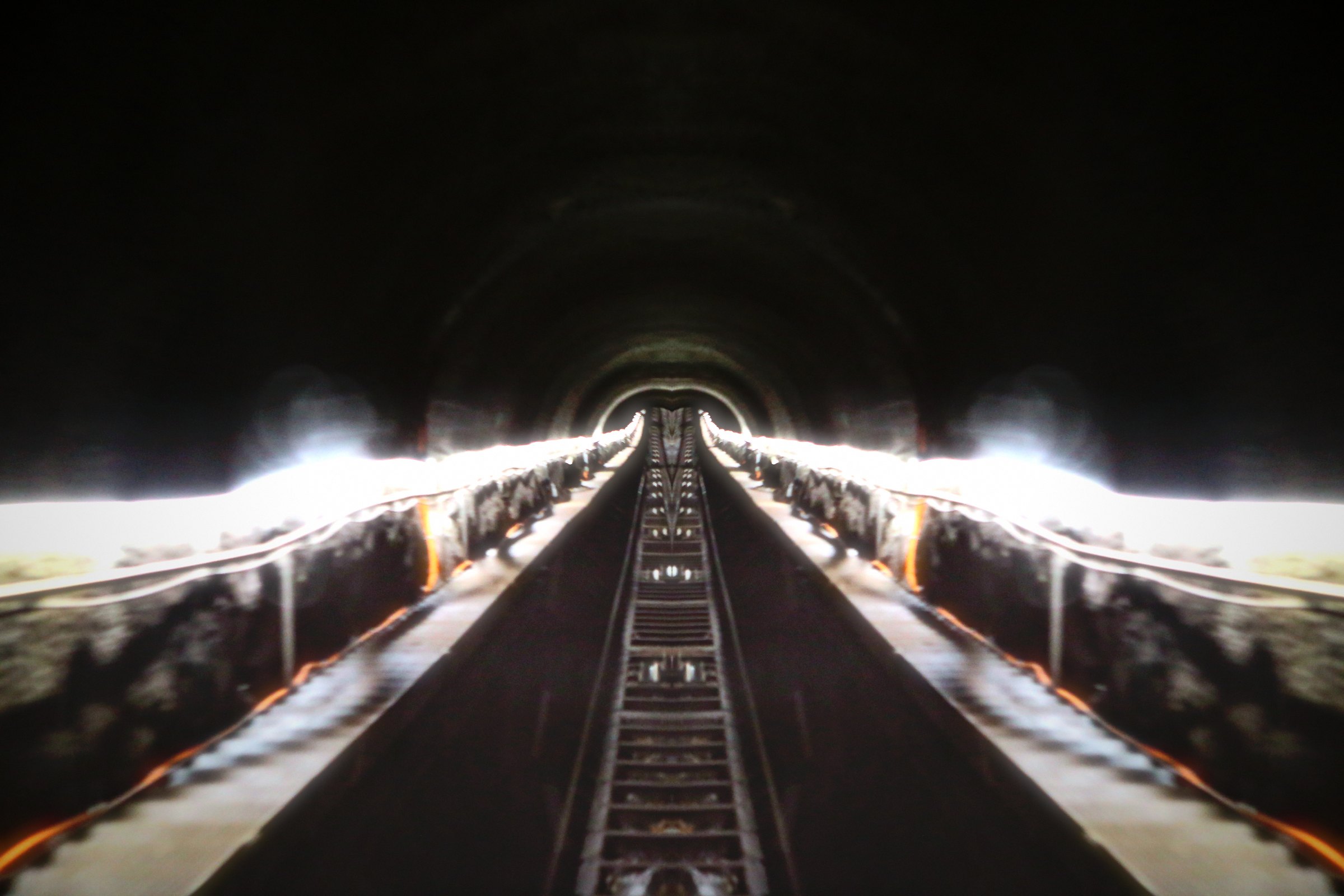Mirrored tunnel with lit platforms on both sides and a track down the middle.