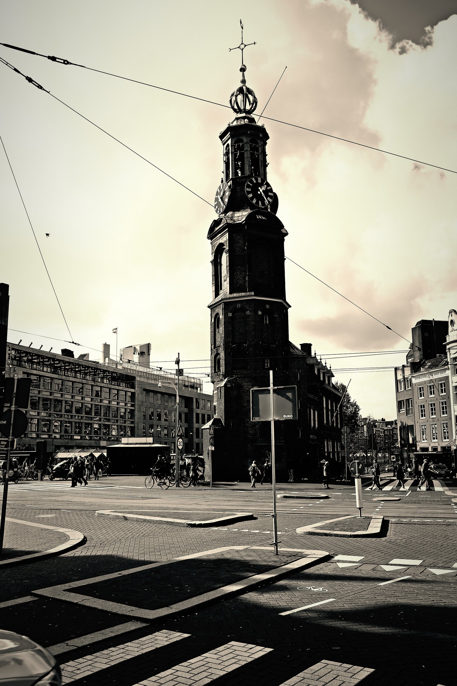 Split-toned clock tower above a tram crossing with wires overhead.