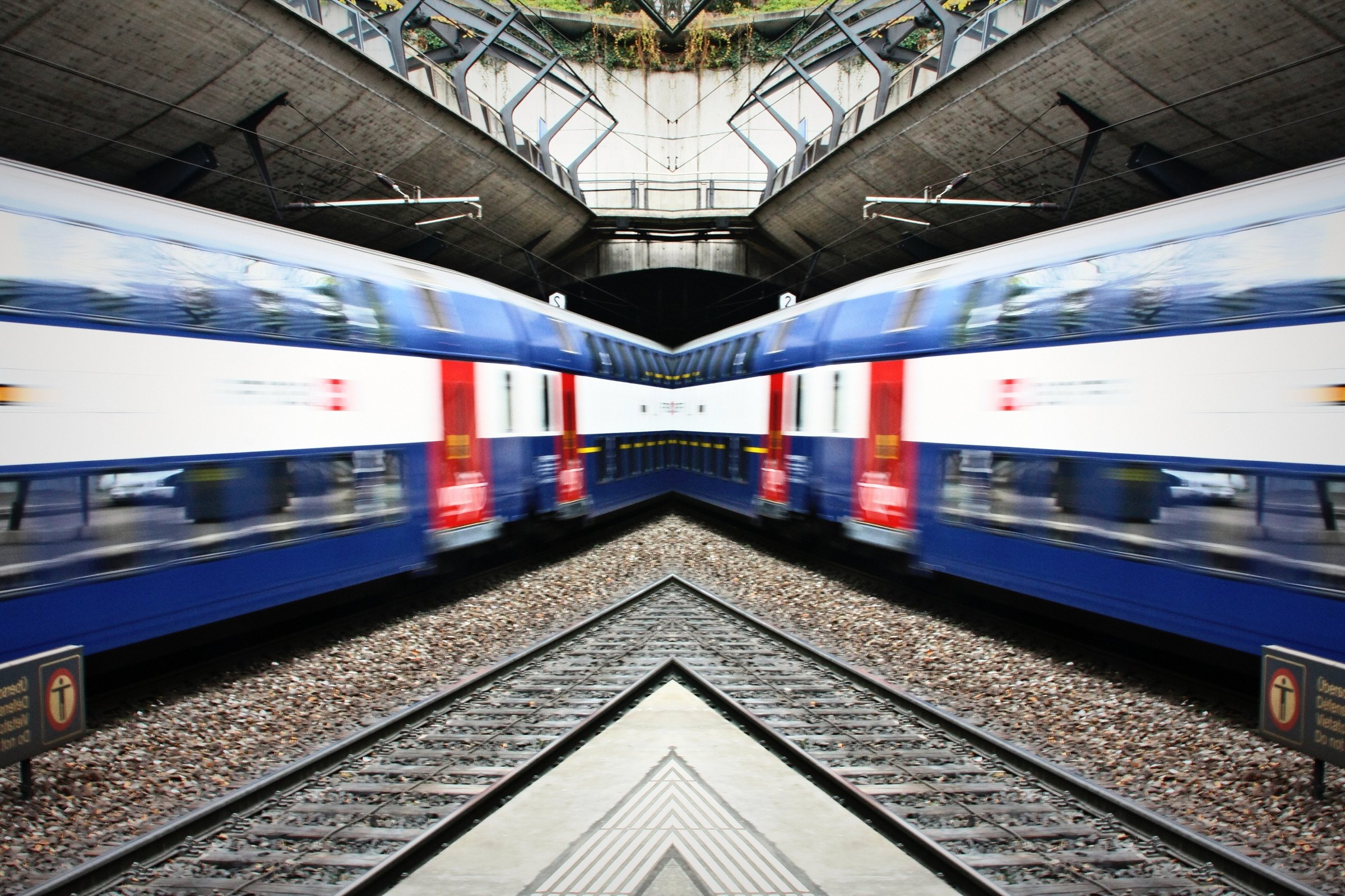 Mirrored image of two blue double-deck trains meeting under a canopy.