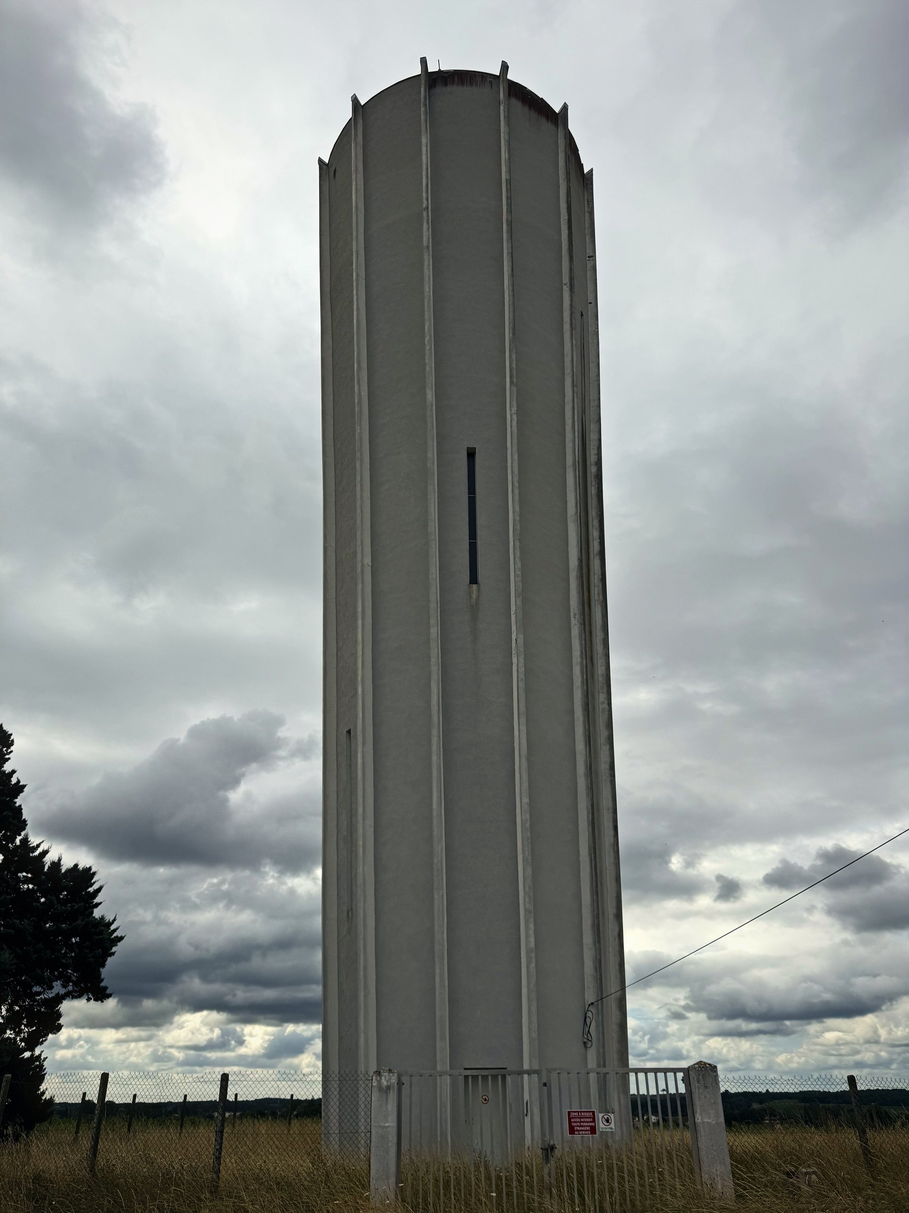 A tall concrete village water tower rising from the fields against a grey, broken sky.