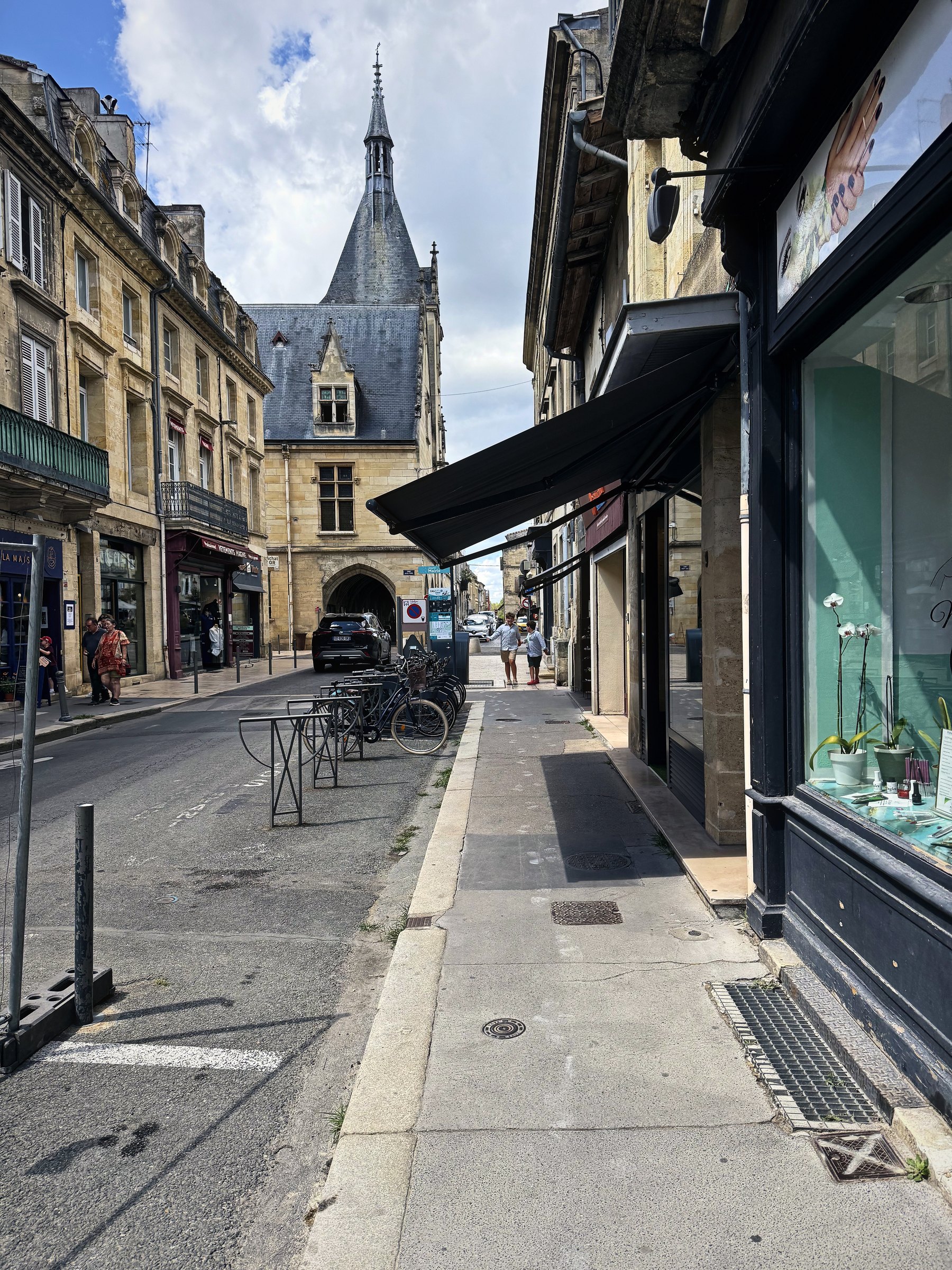 A town street leading to a tall clock gate tower with shopfronts and a wide pavement.