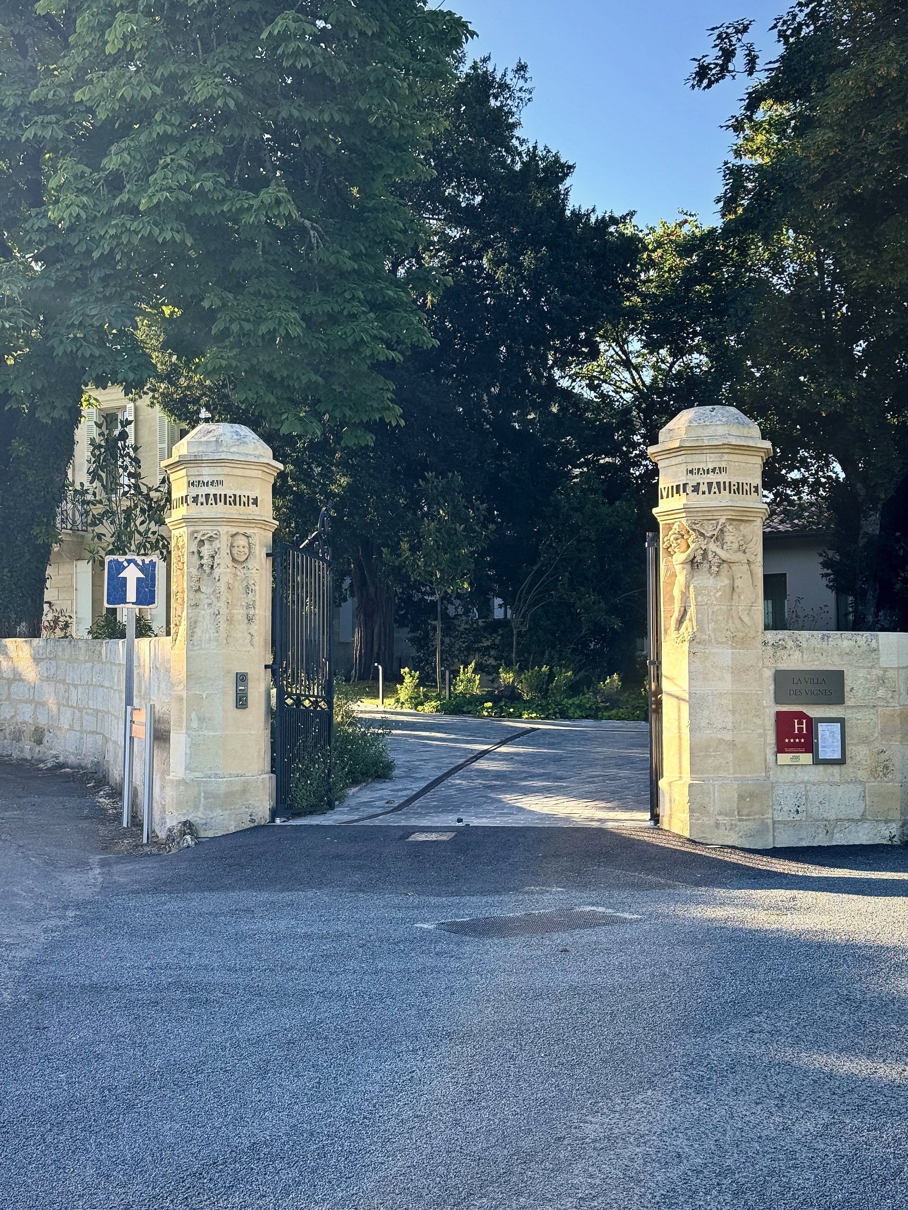 Two pale stone gateposts at the entrance to a tree-shaded lane.